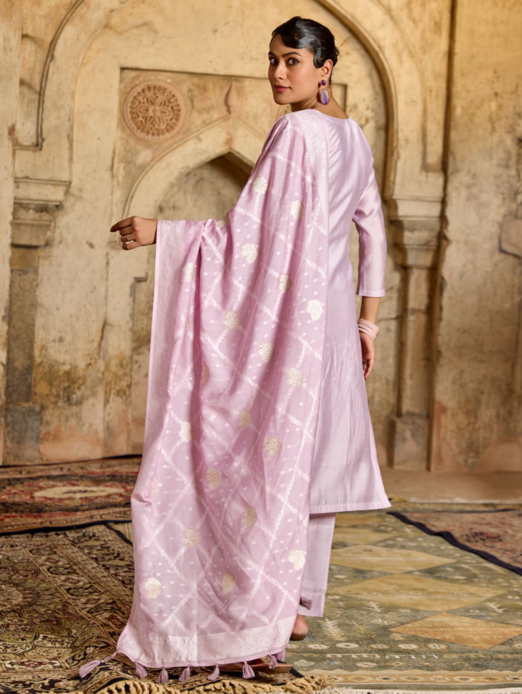 A woman wearing a pink viscose silk suit set with embroidered details, consisting of a kurta, pants, and a jacquard weave silk dupatta.