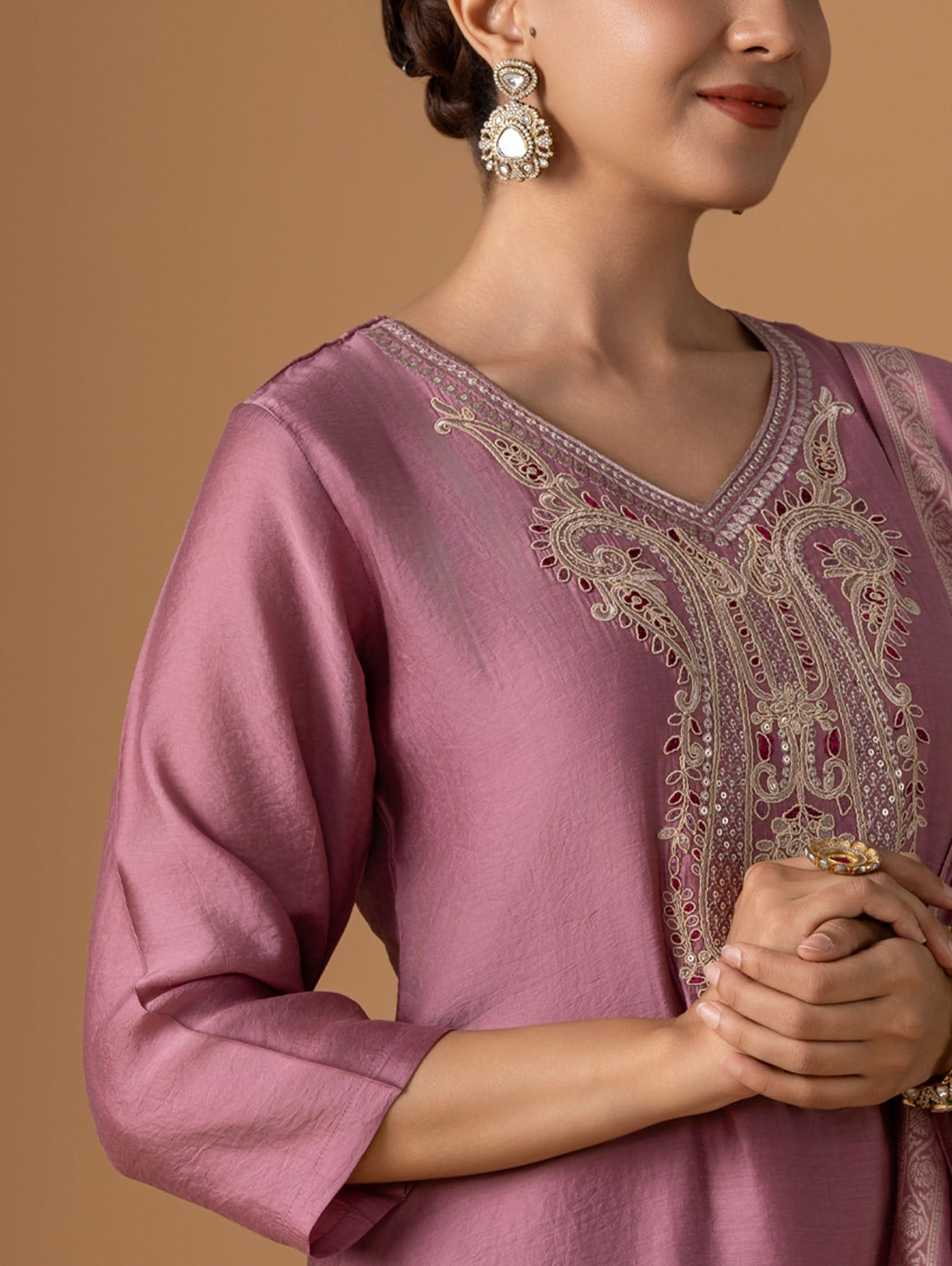 Woman wearing a pink embroidered traditional outfit with a beige background