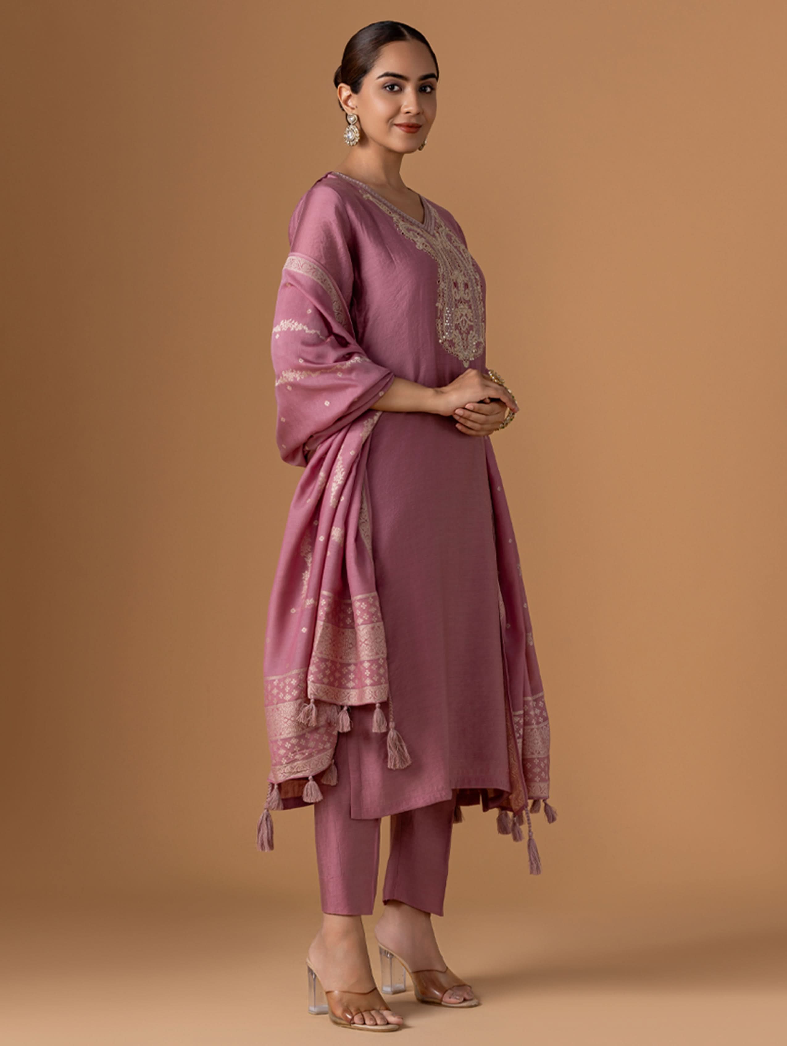 Woman wearing a mauve traditional outfit with intricate patterns on a beige background