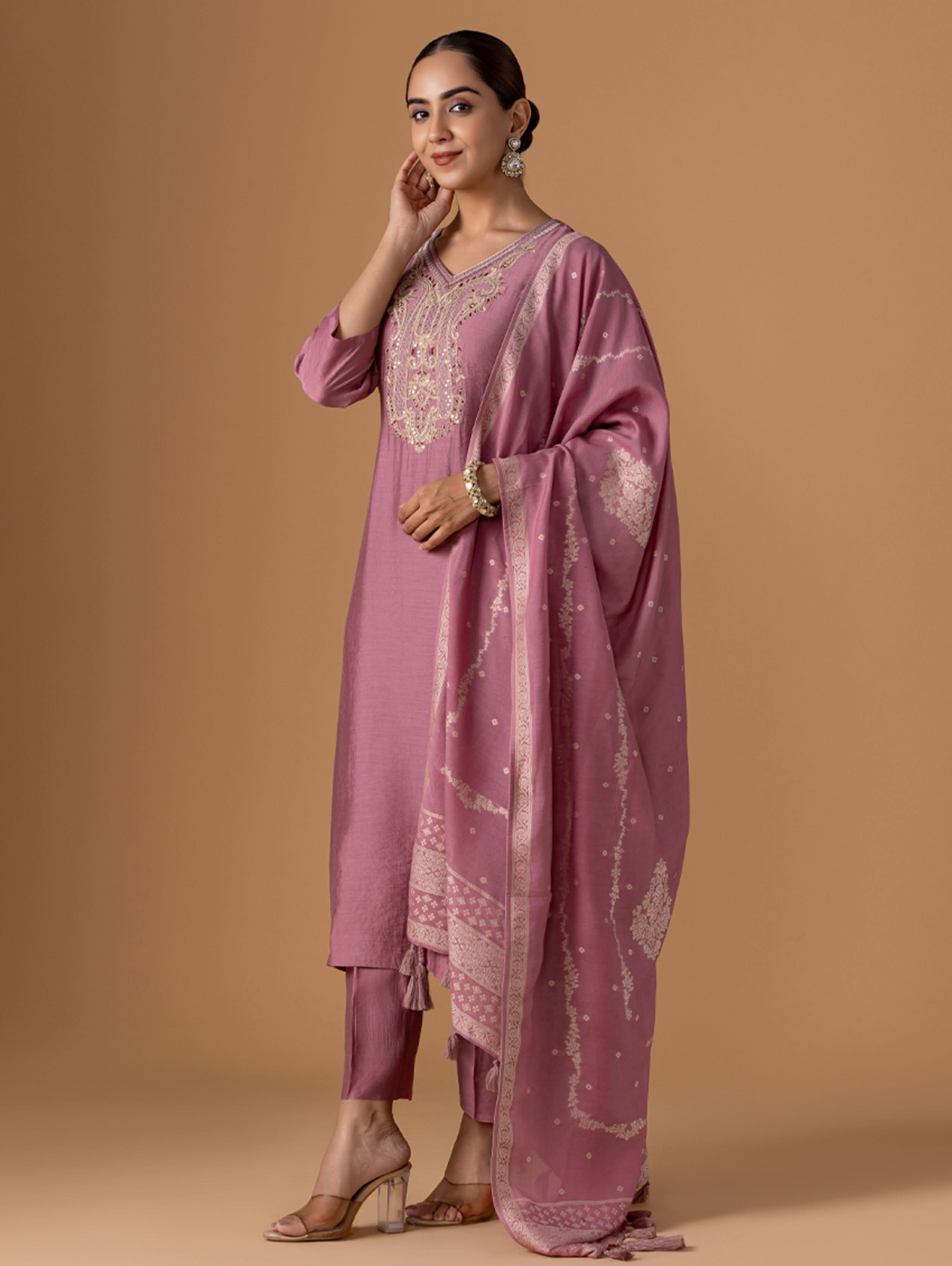 Woman wearing a pink traditional outfit with a matching dupatta against a beige background