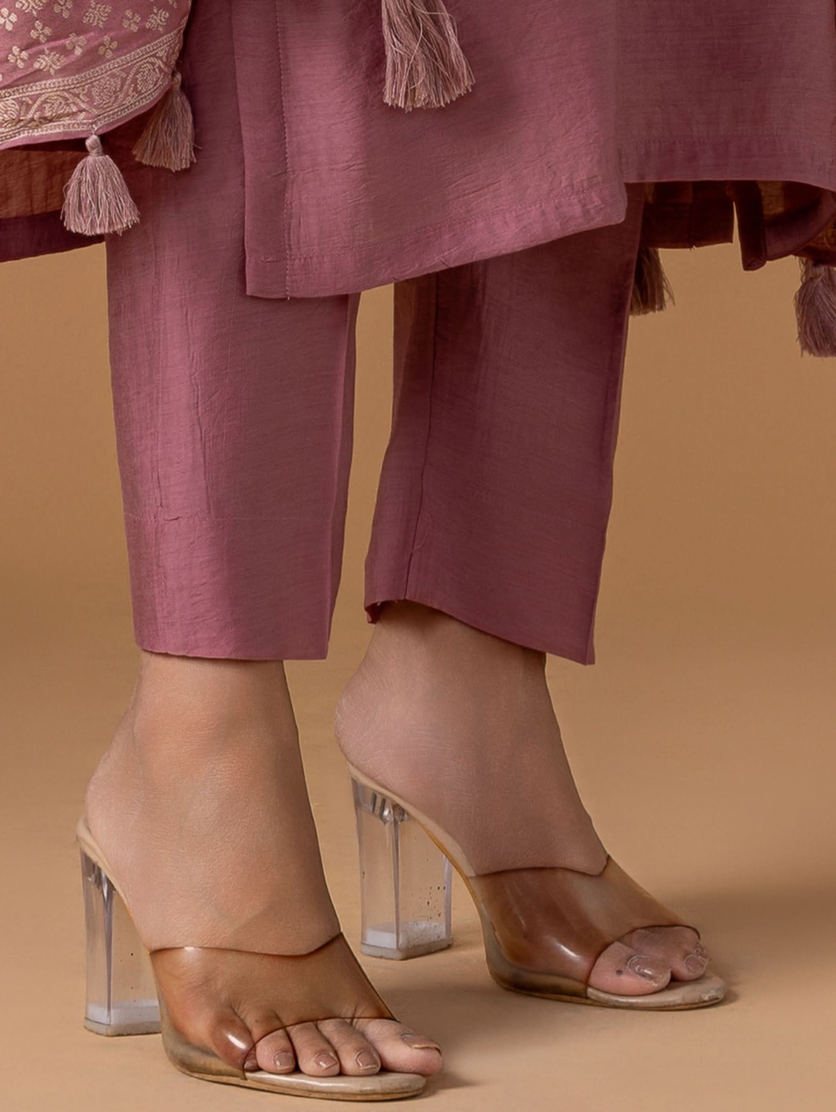 Person wearing pink traditional outfit with transparent high-heeled shoes on a beige background