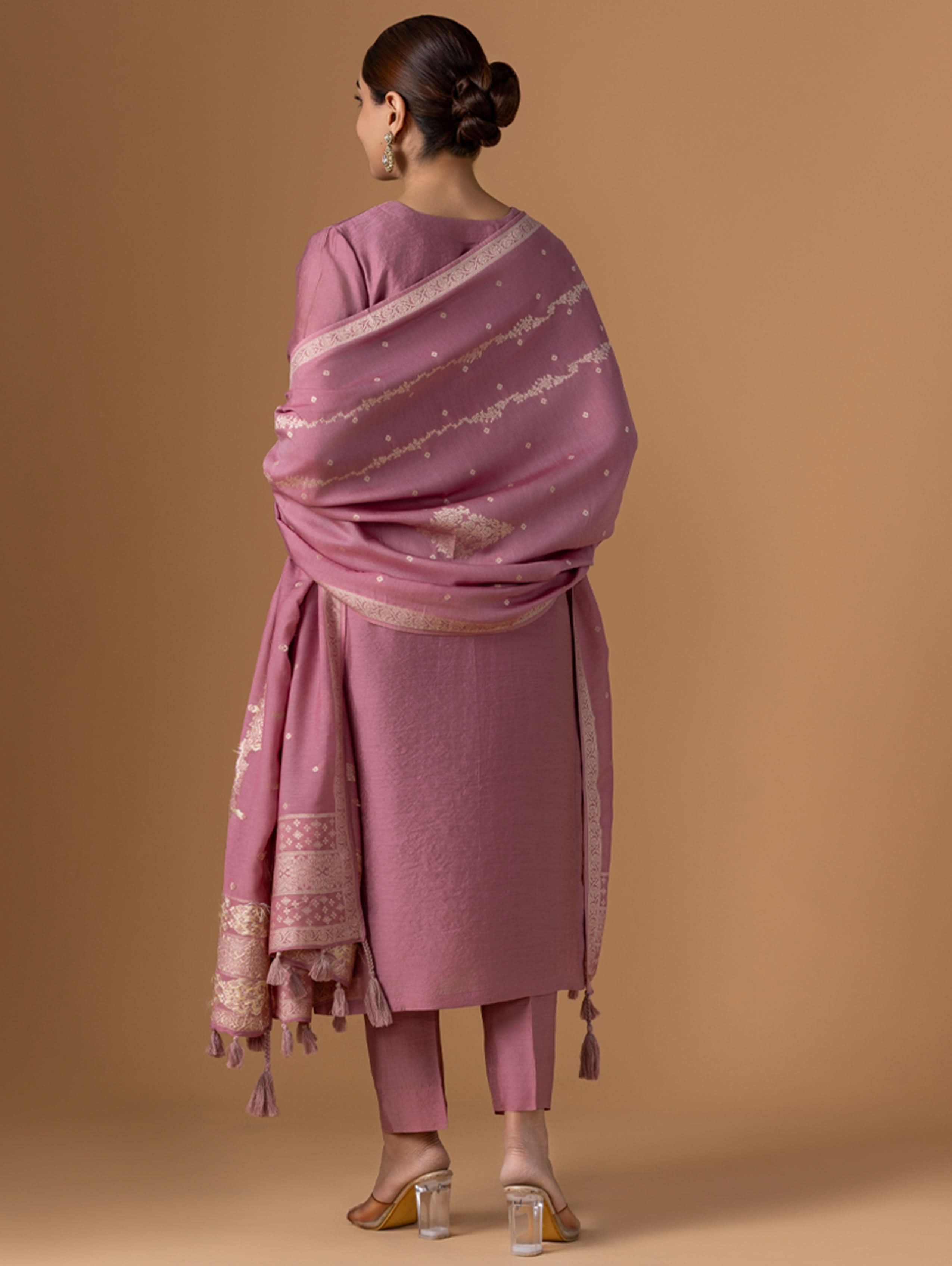 Woman wearing a pink traditional outfit with a matching dupatta on a brown background