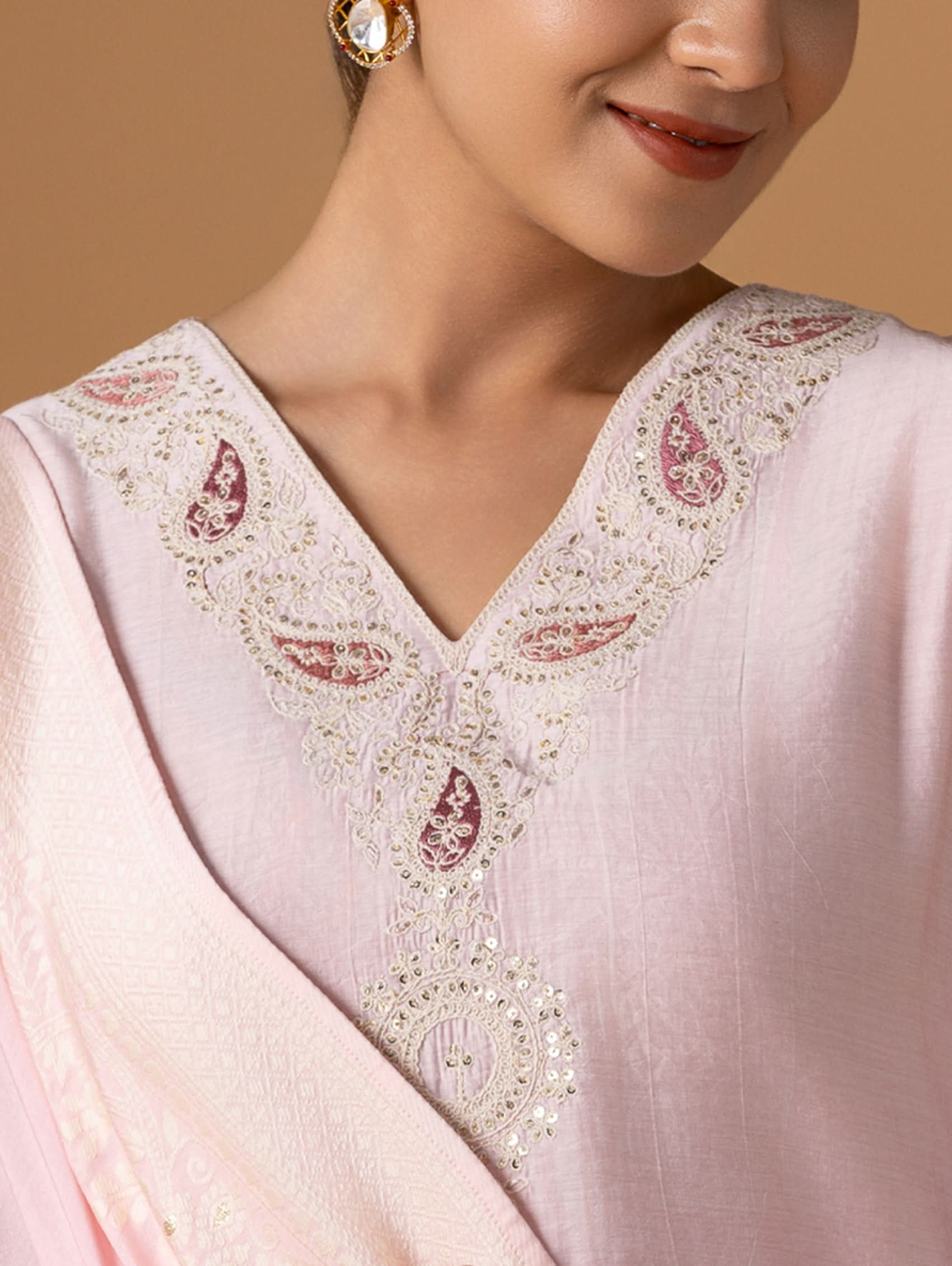 Close-up of a pink traditional outfit with intricate white embroidery on a beige background