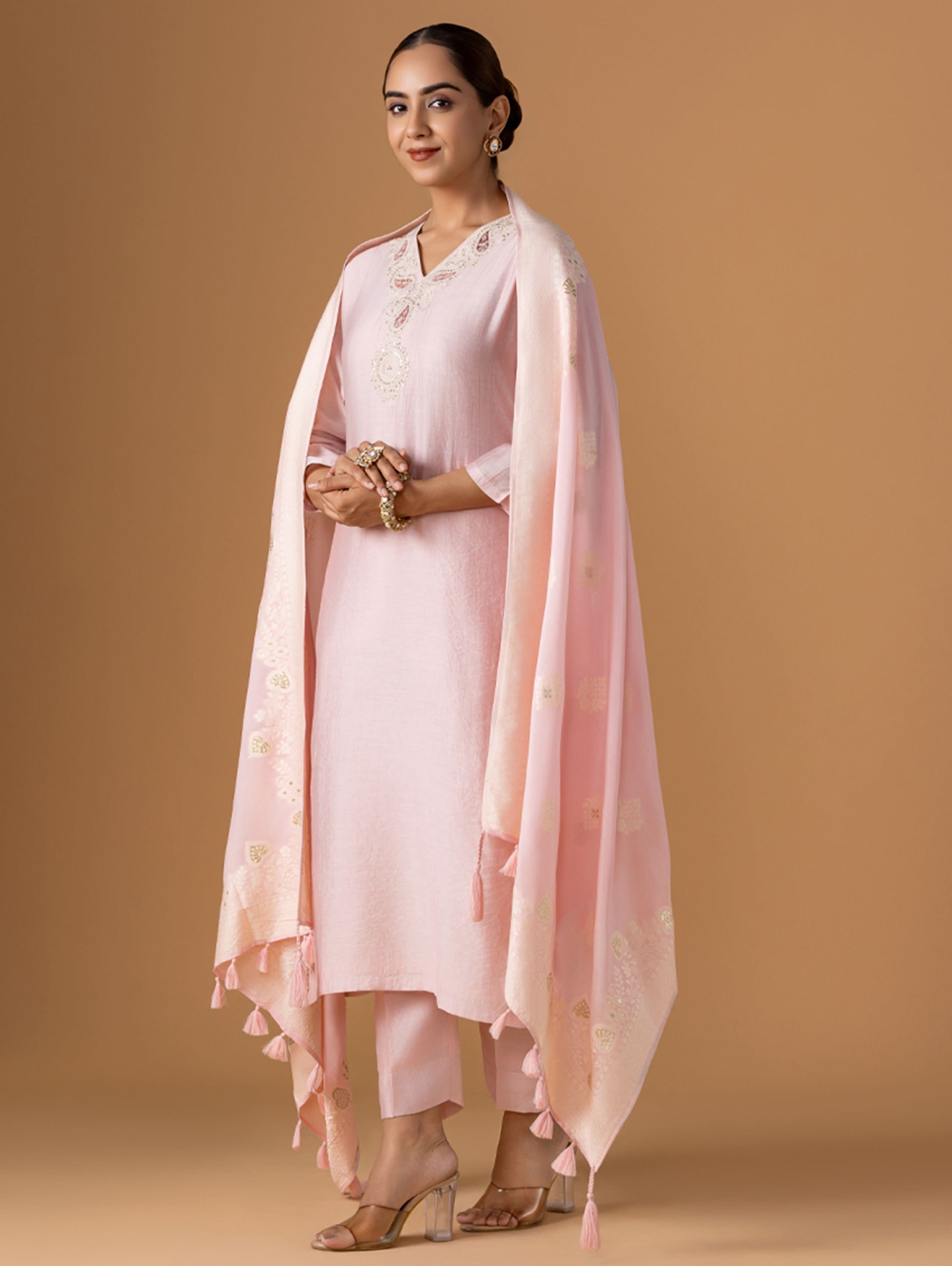 Woman wearing a light pink traditional outfit with a matching dupatta against a beige background