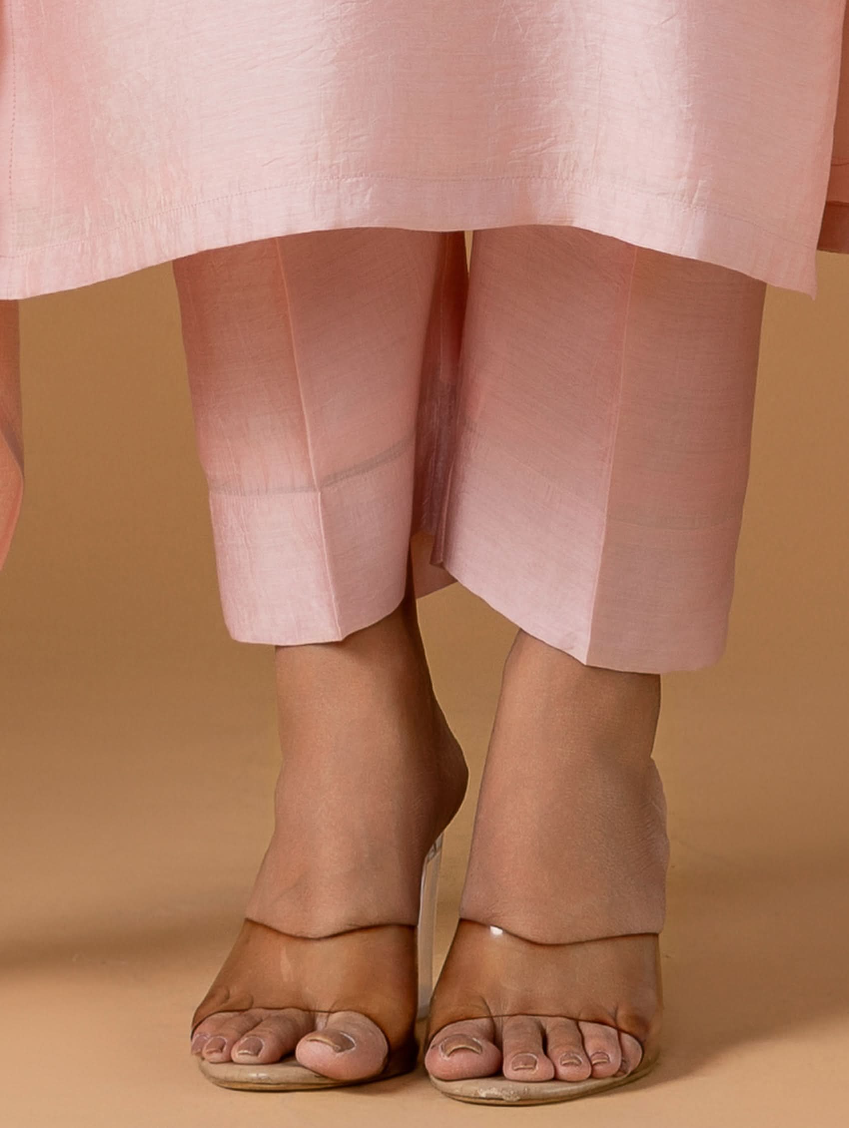 Person wearing light pink pants and sandals on a beige background