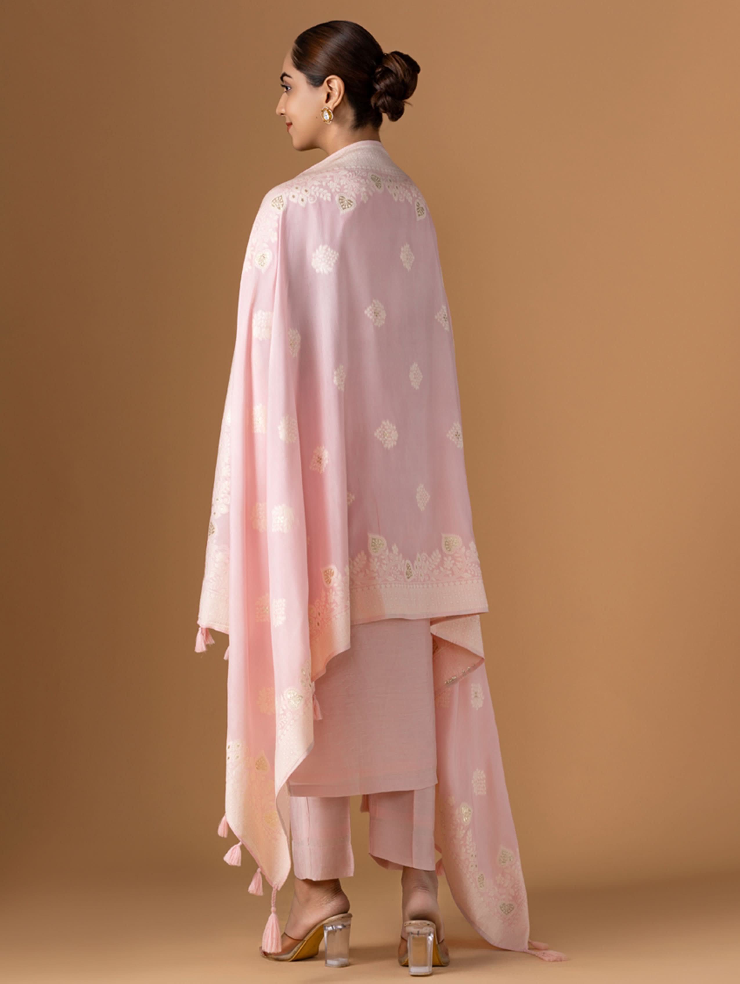 Woman wearing a light pink traditional outfit with a matching dupatta against a brown background