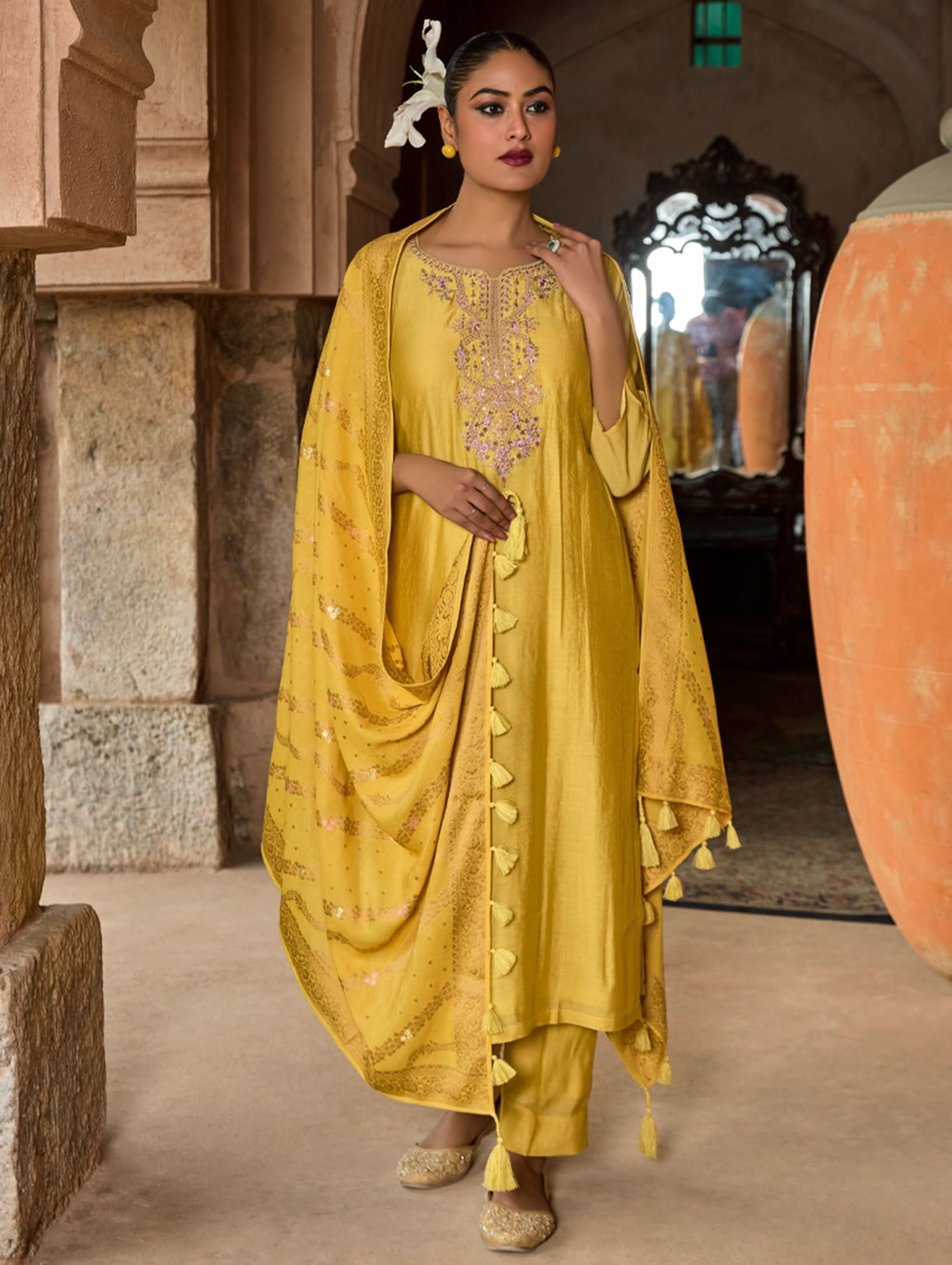 A woman wearing a yellow viscose suit set with embroidery, consisting of a kurta, pants, and a jacquard weave silk dupatta.