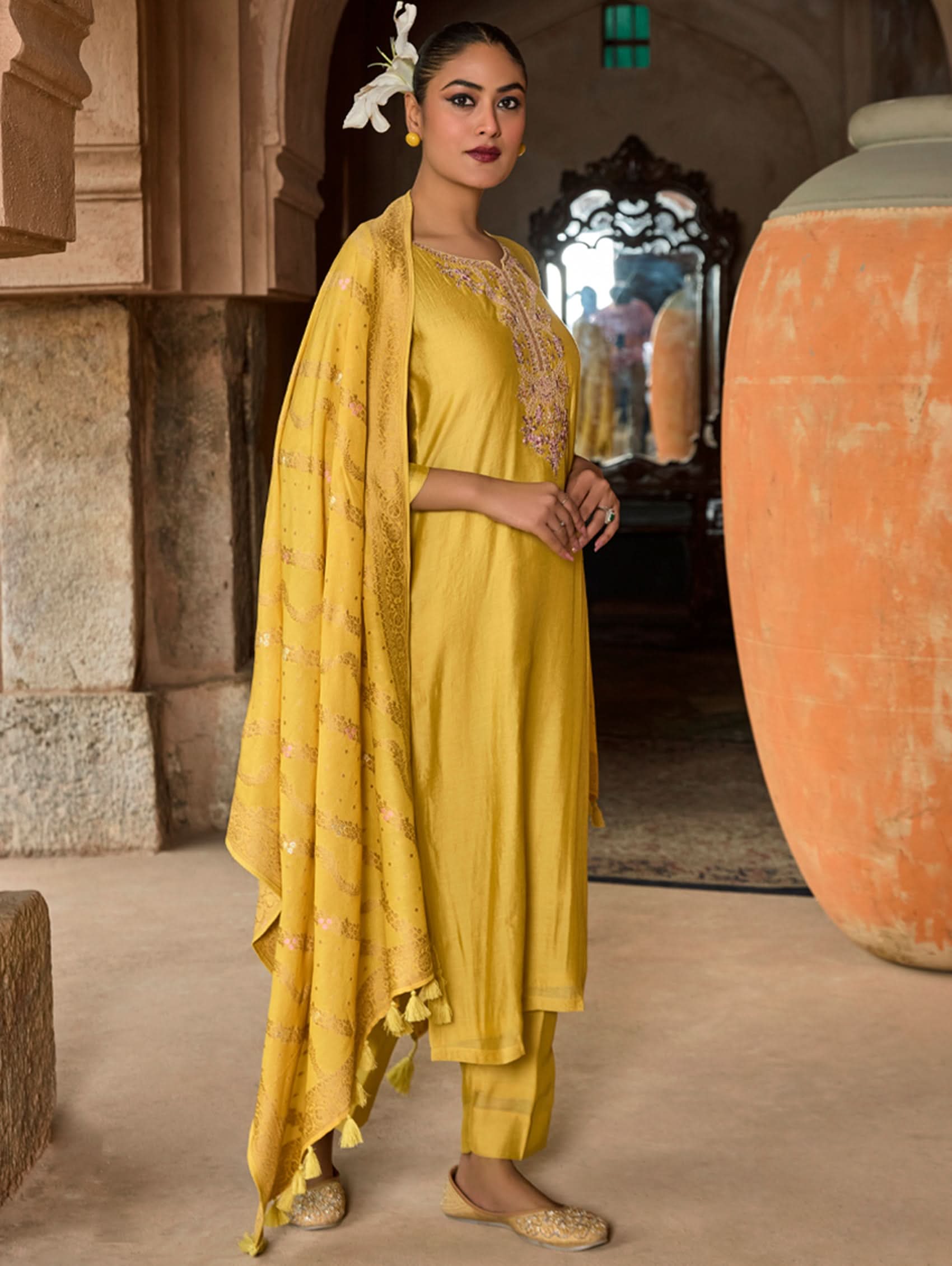 Woman in a yellow traditional outfit standing in a historical setting.