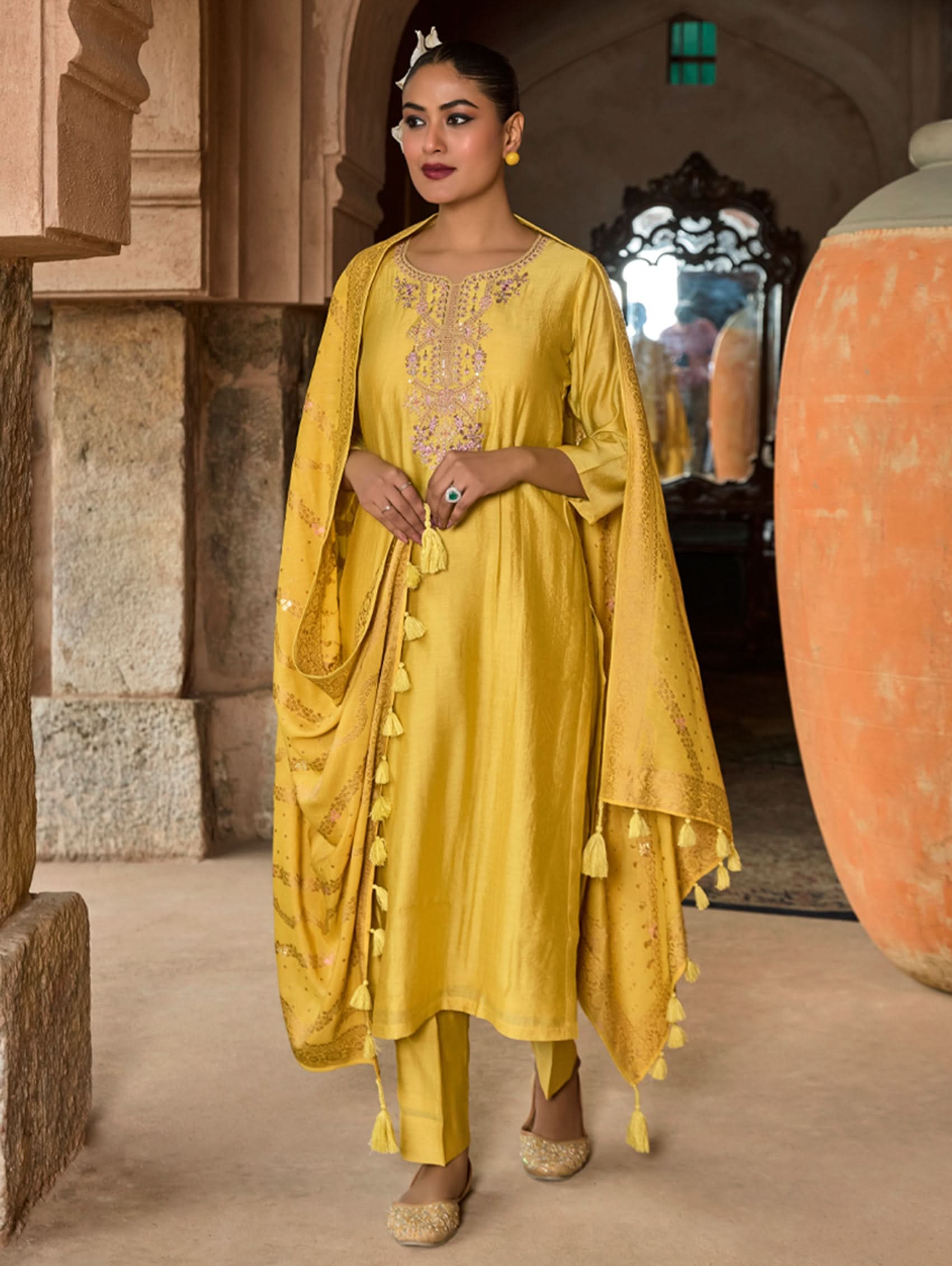 Woman in a yellow traditional outfit standing in a stone archway.