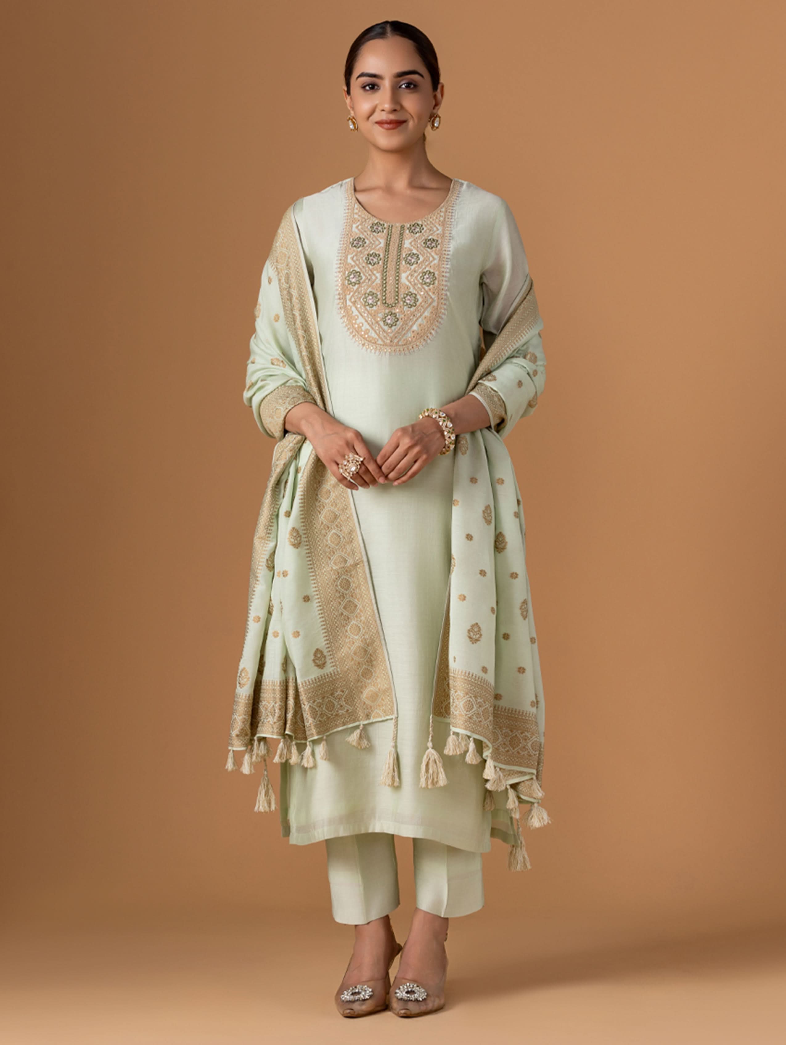 Woman wearing a light green embroidered outfit with a beige background