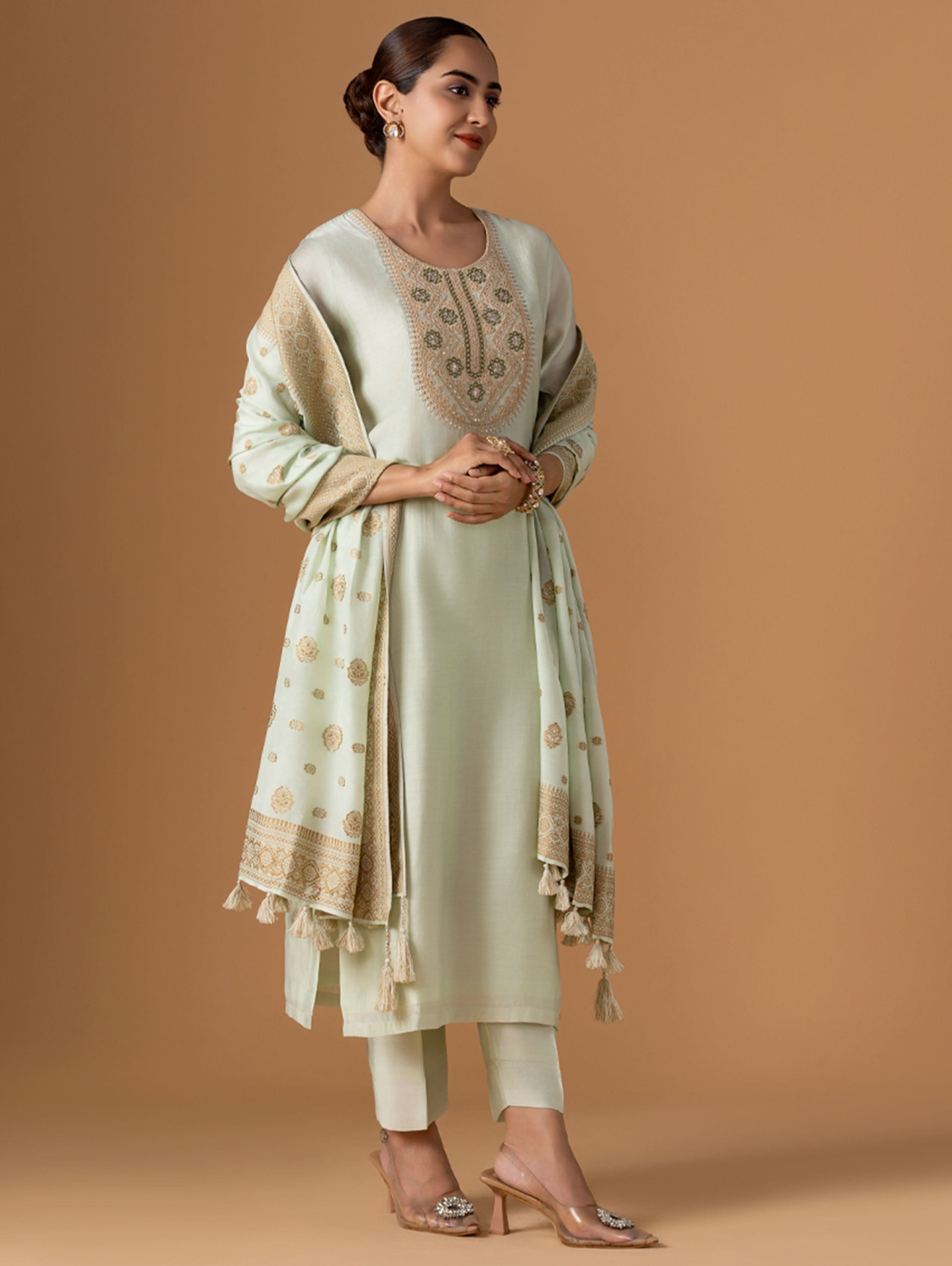 Woman wearing a light green traditional outfit with a beige dupatta against a brown background