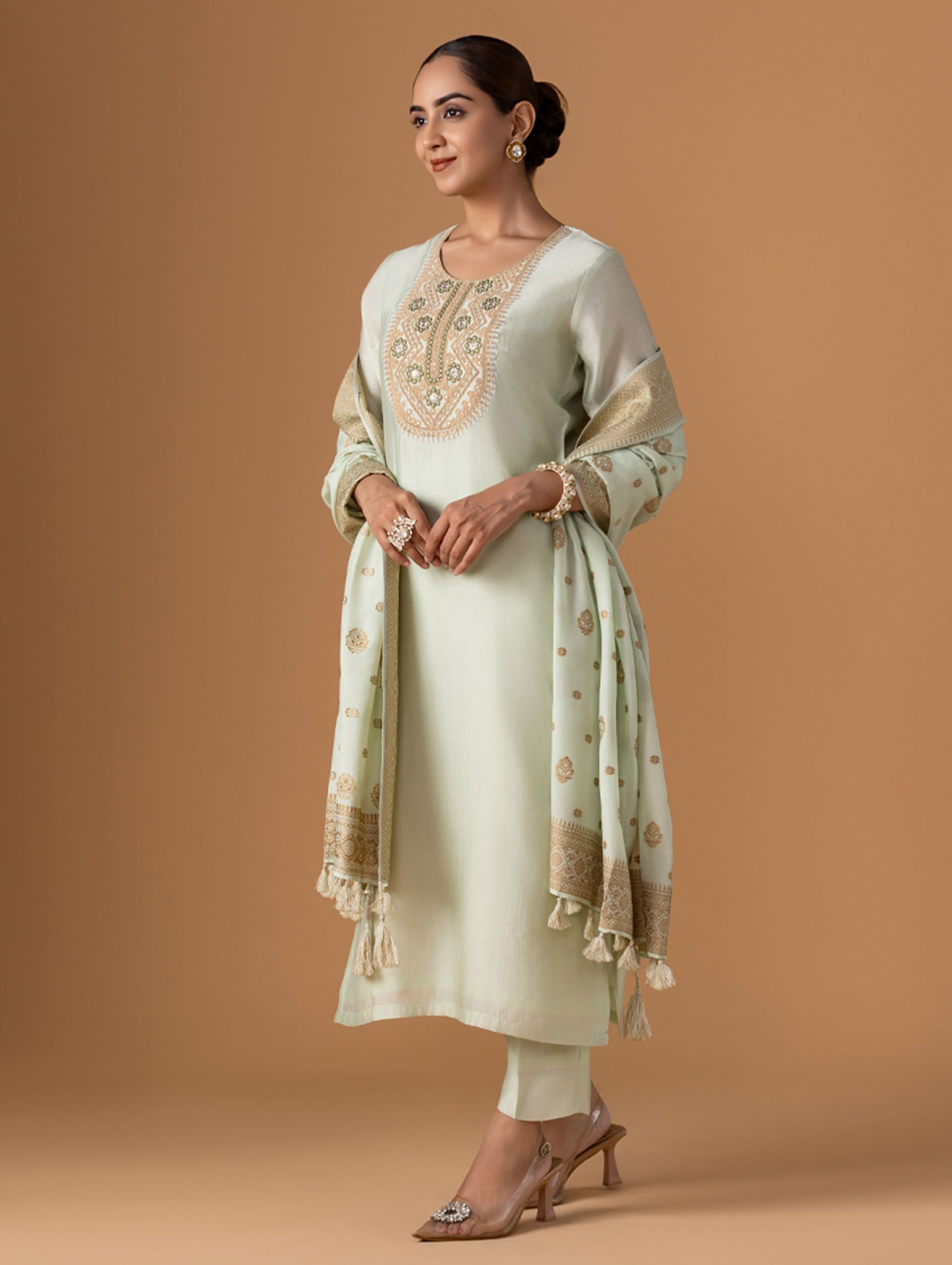 Woman wearing a light green traditional outfit with a matching dupatta on a brown background