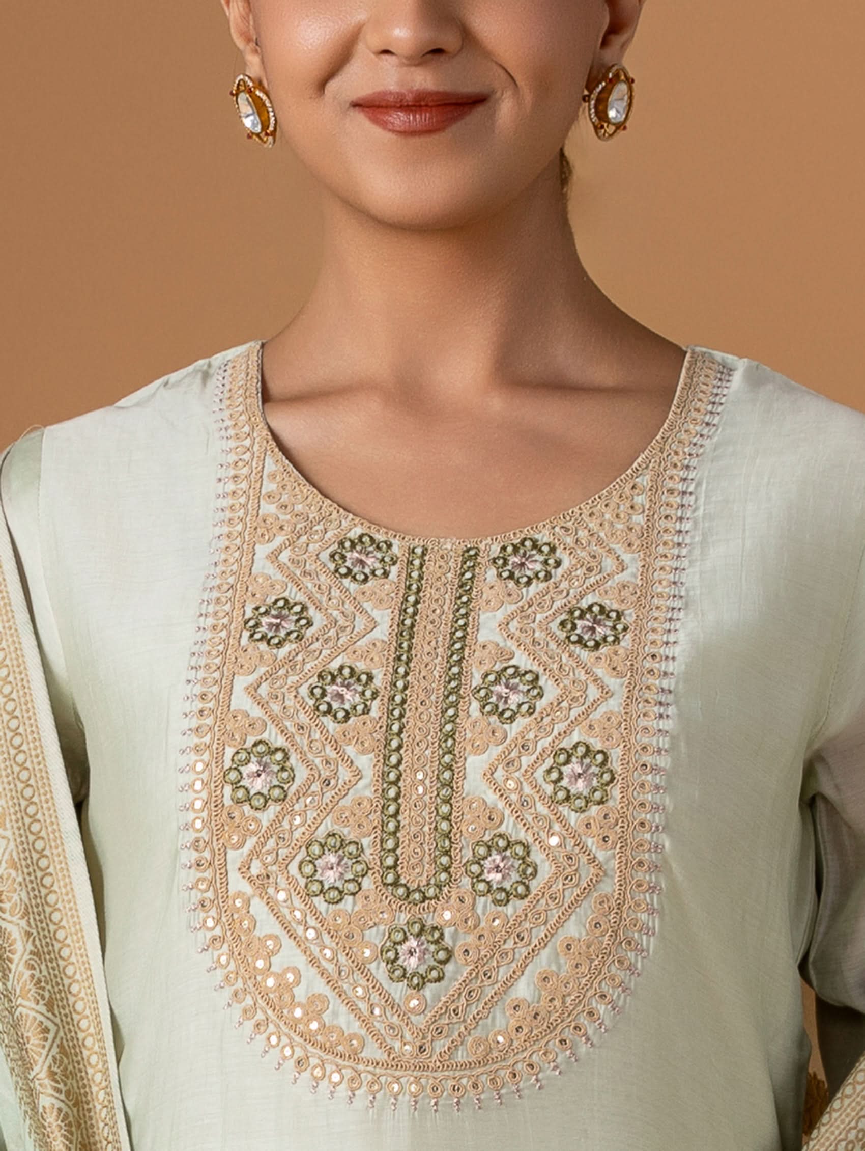 Close-up of a person wearing a light-colored embroidered top with a neutral background