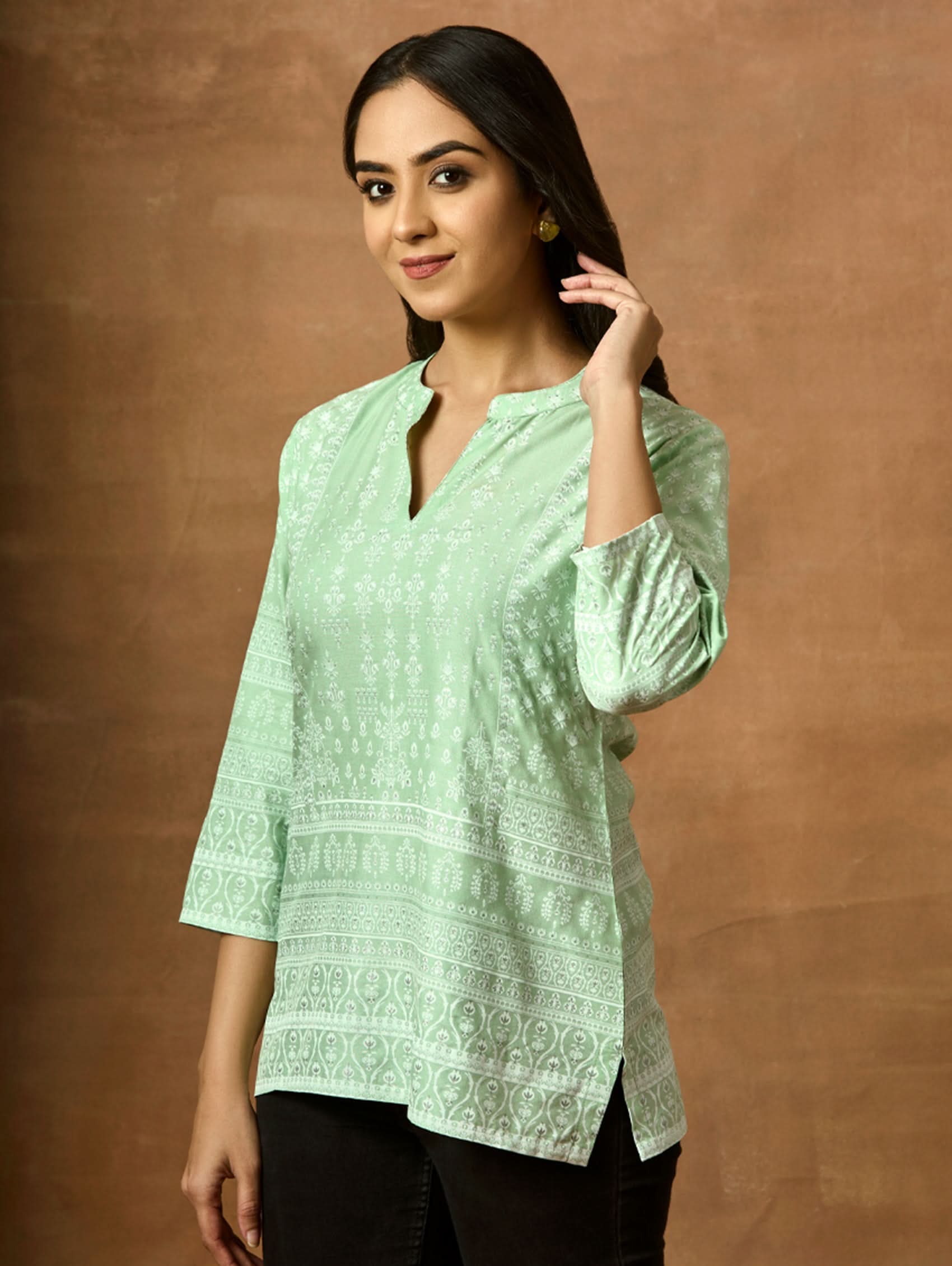 A woman wearing a Green printed viscose rayon tunic with a ban collar and three-fourth sleeves, paired with white trousers.