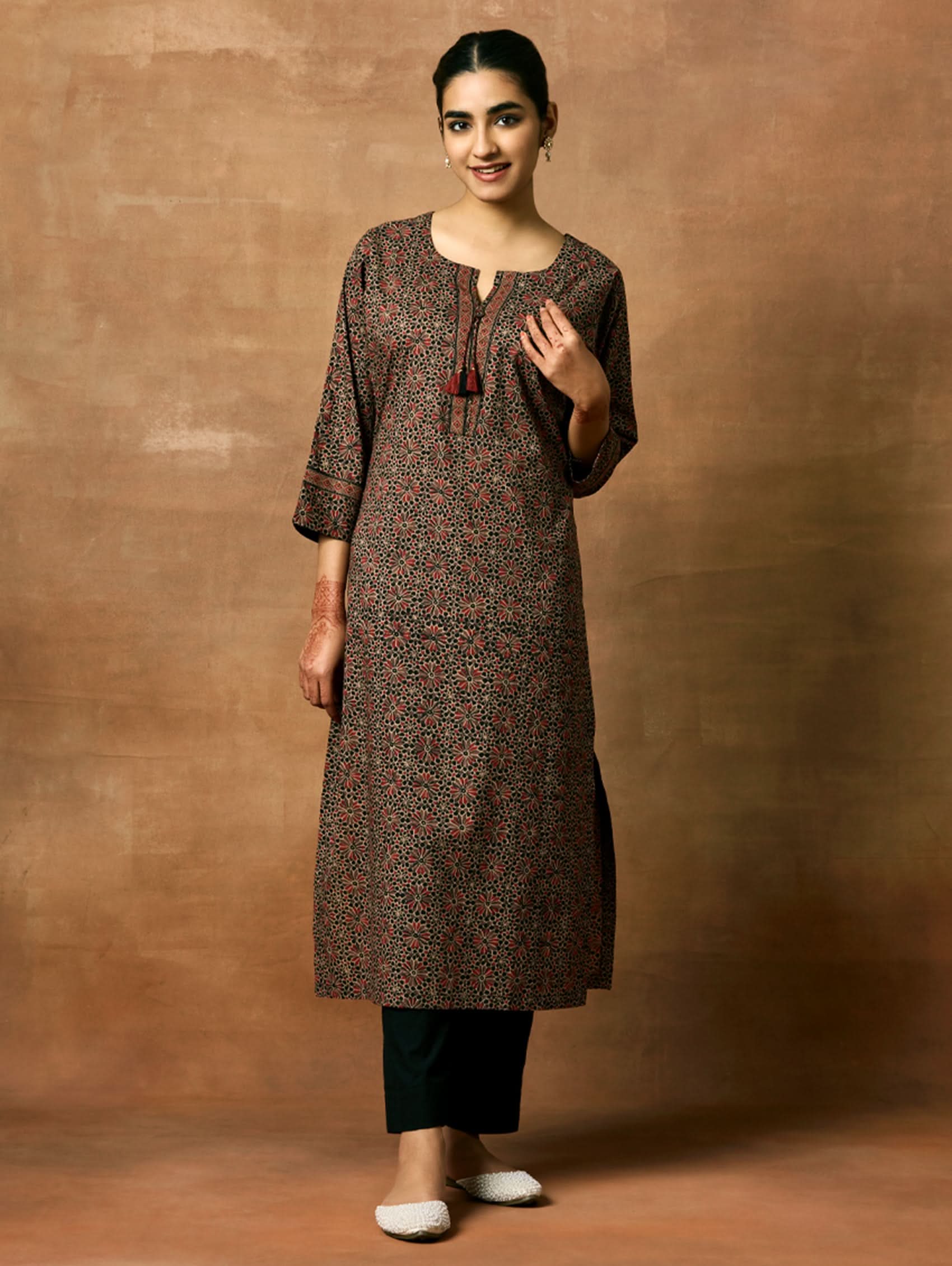 A woman plus-size model wearing a knee-length cotton kurta with a round neckline, three-fourth sleeves, and side slits. The kurta has a round neckline with tassels and is printed with a small floral pattern.