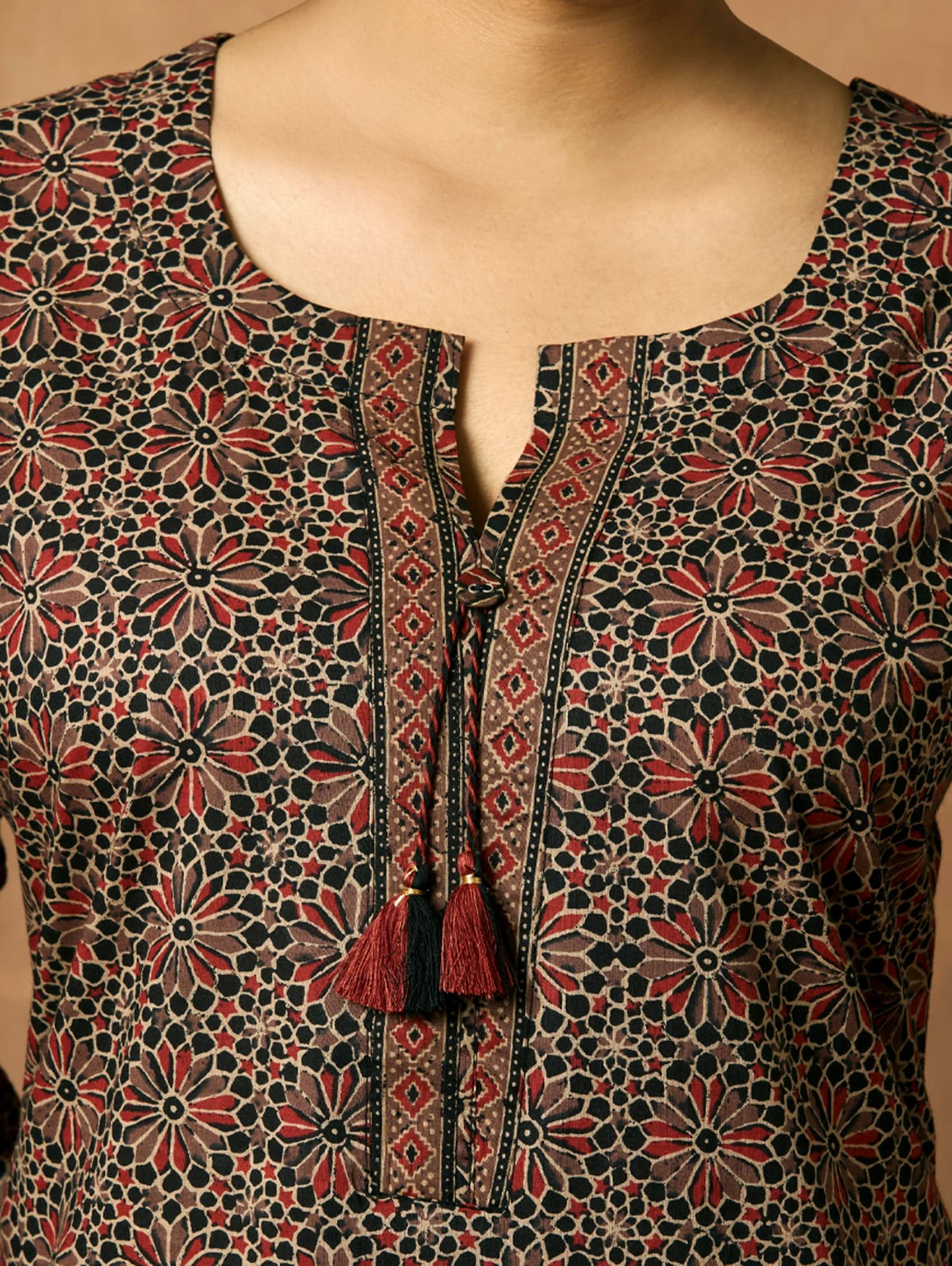 A woman plus-size model wearing a knee-length cotton kurta with a round neckline, three-fourth sleeves, and side slits. The kurta has a round neckline with tassels and is printed with a small floral pattern.