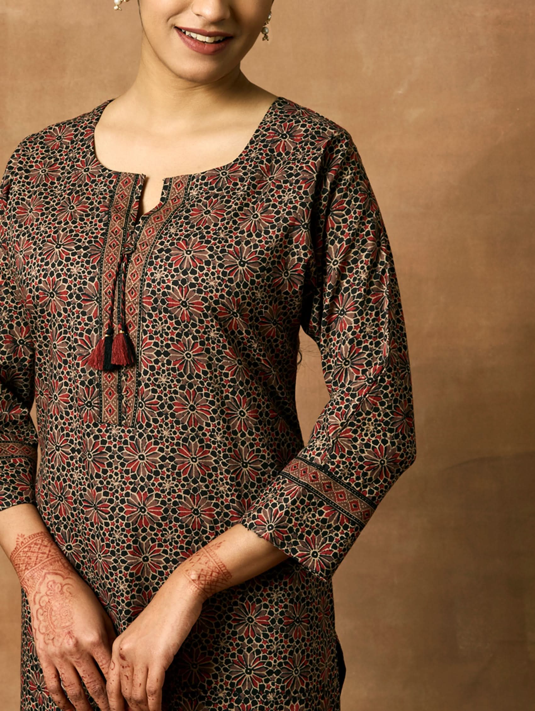 A woman plus-size model wearing a knee-length cotton kurta with a round neckline, three-fourth sleeves, and side slits. The kurta has a round neckline with tassels and is printed with a small floral pattern.