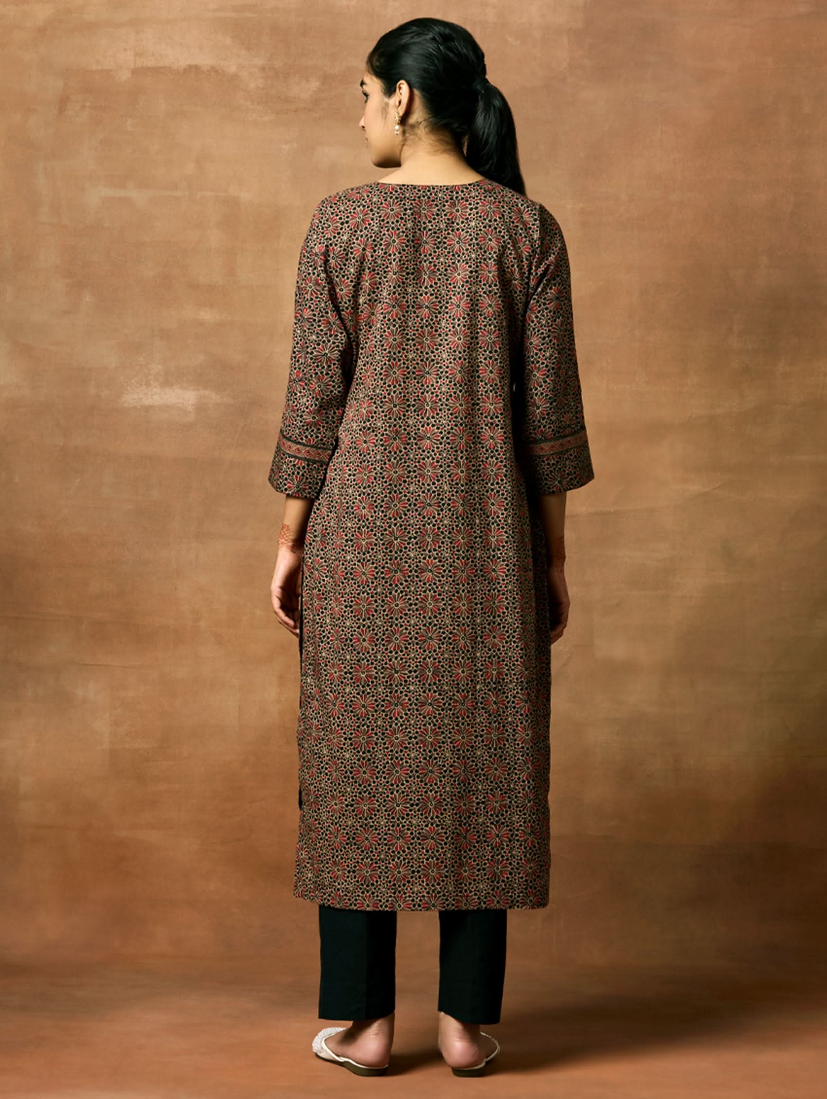 A woman plus-size model wearing a knee-length cotton kurta with a round neckline, three-fourth sleeves, and side slits. The kurta has a round neckline with tassels and is printed with a small floral pattern.