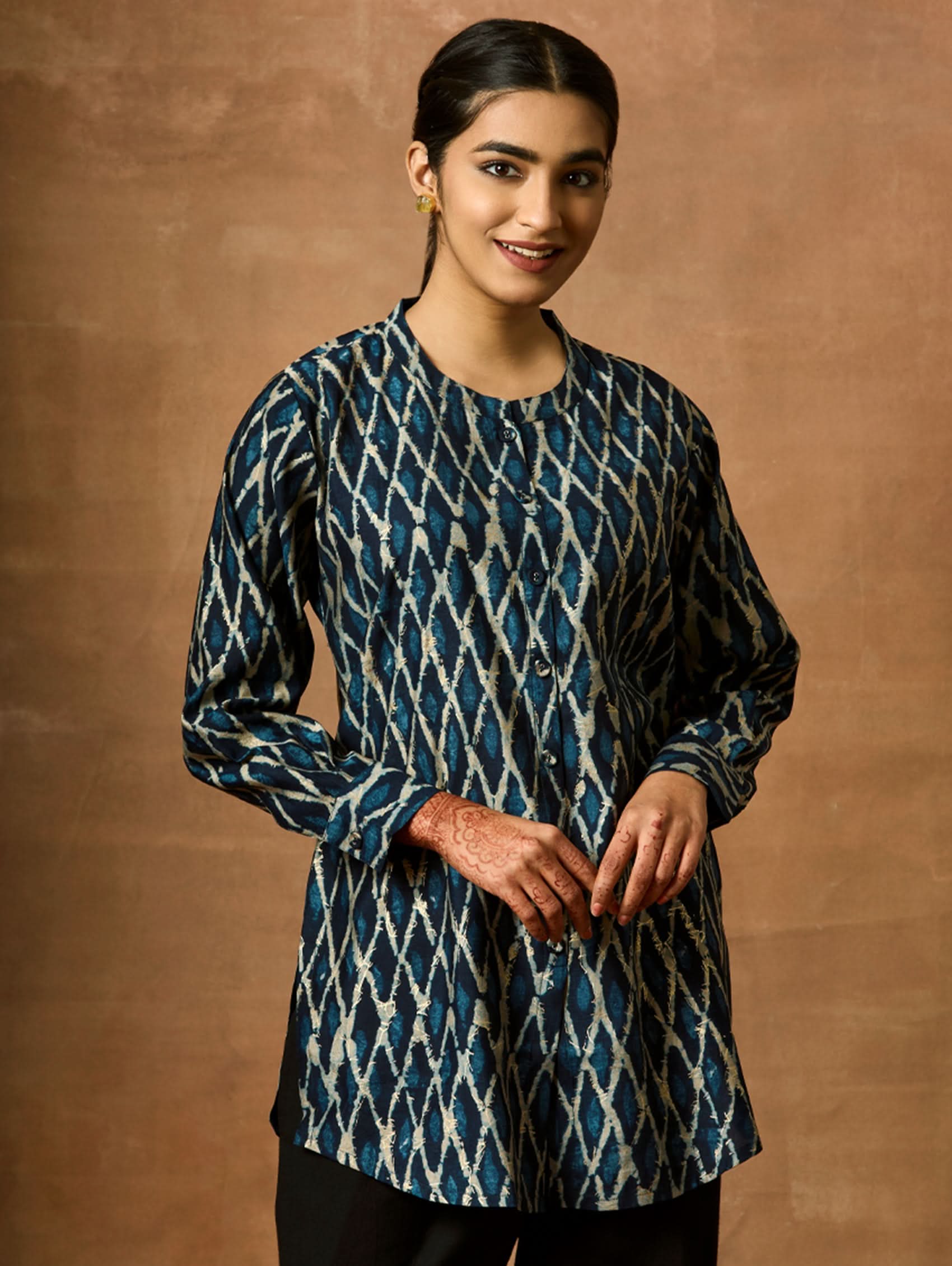 A woman wearing a short kurti with a mandarin collar, full sleeves, and side slits. The kurti is printed with a geometric pattern.