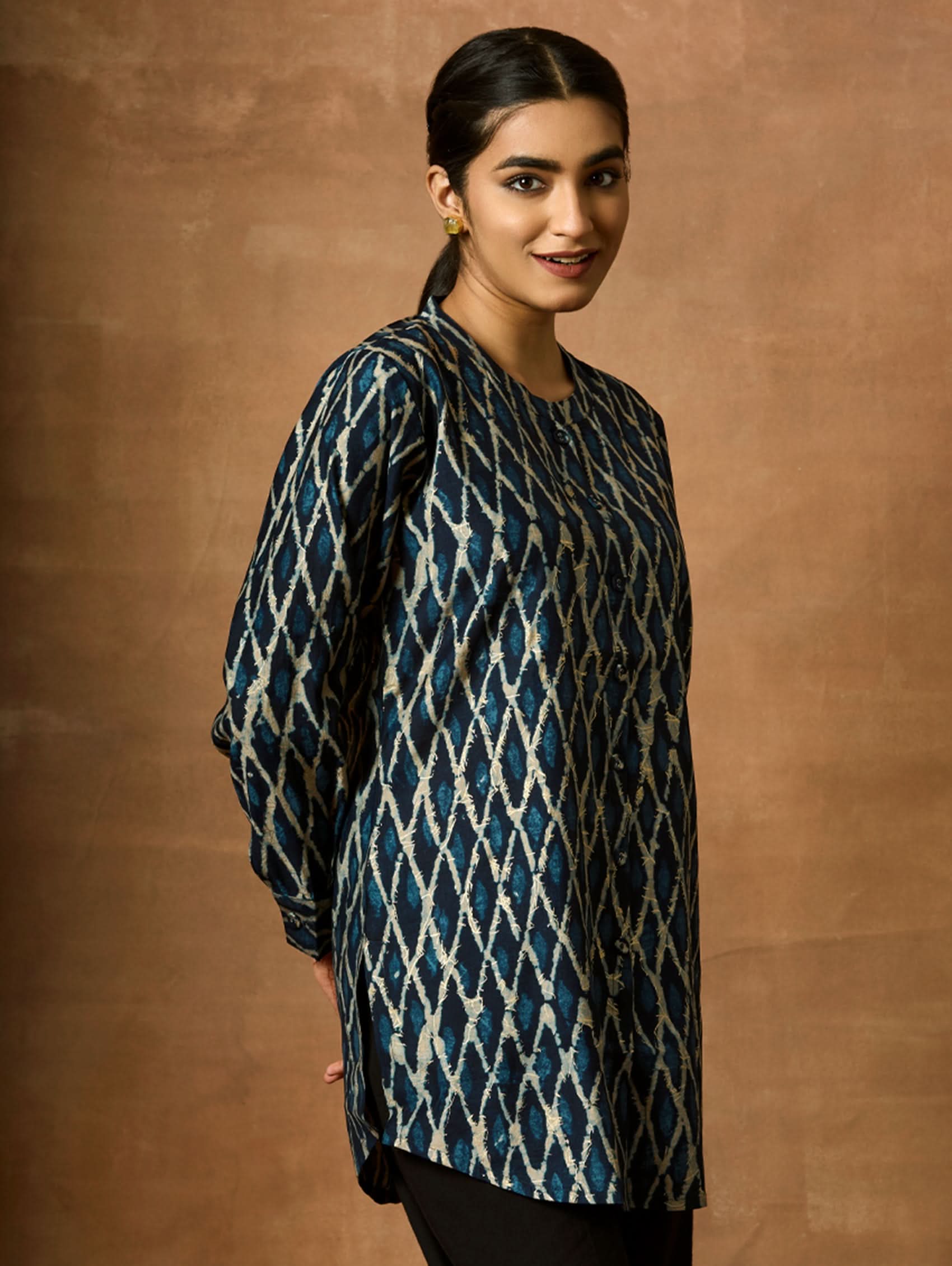 A woman wearing a short kurti with a mandarin collar, full sleeves, and side slits. The kurti is printed with a geometric pattern.