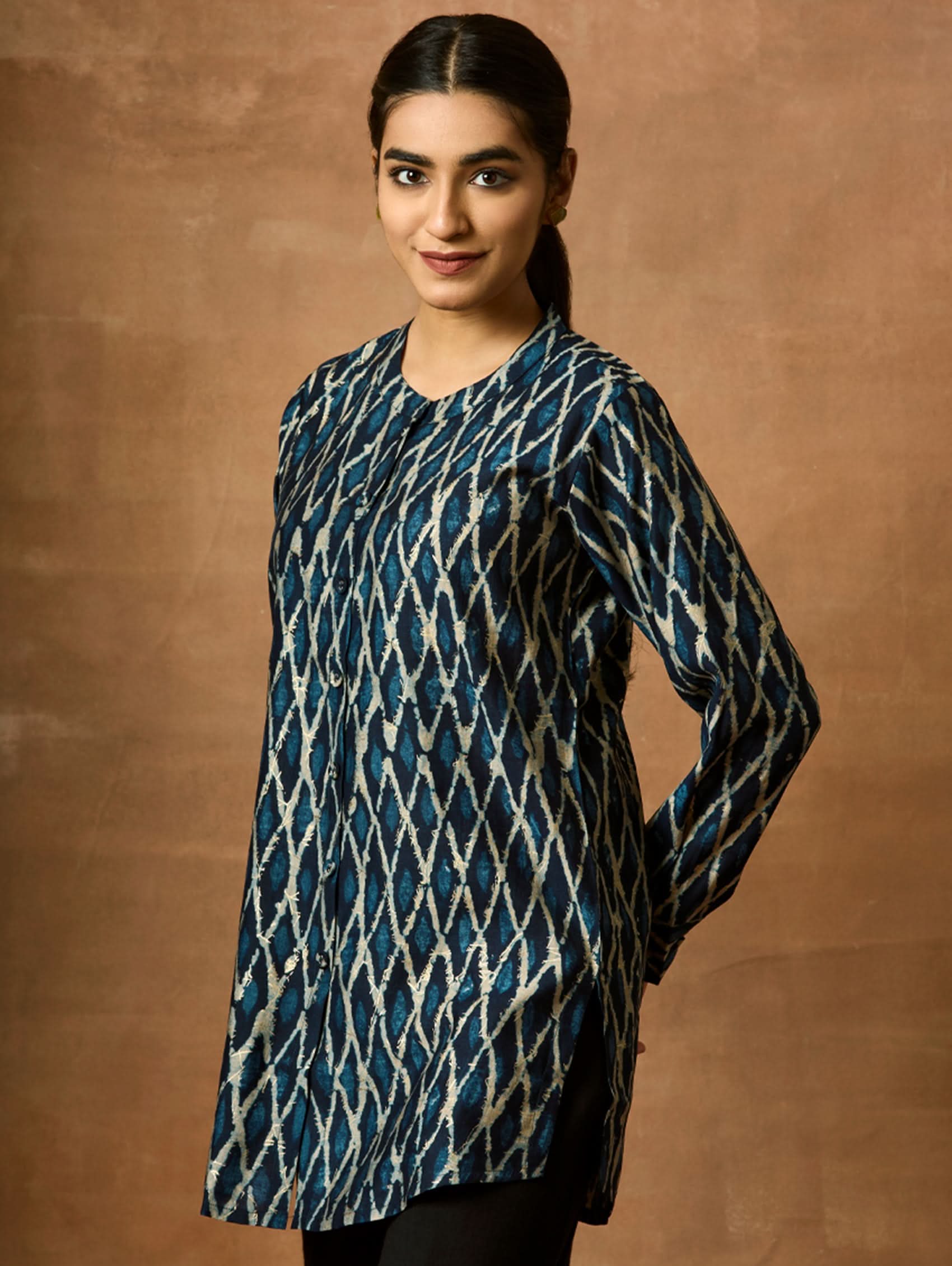A woman wearing a short kurti with a mandarin collar, full sleeves, and side slits. The kurti is printed with a geometric pattern.
