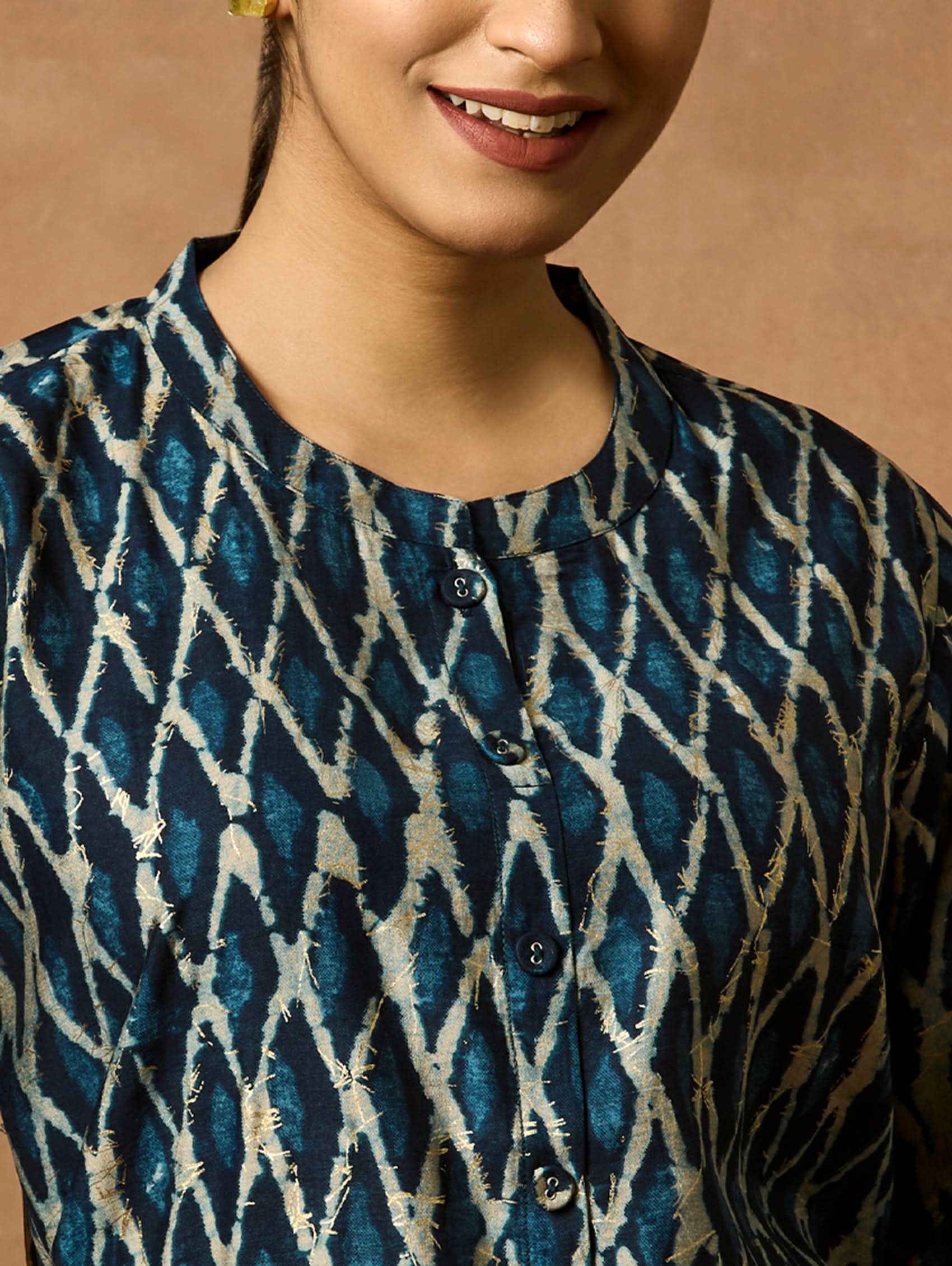 A woman wearing a short kurti with a mandarin collar, full sleeves, and side slits. The kurti is printed with a geometric pattern.
