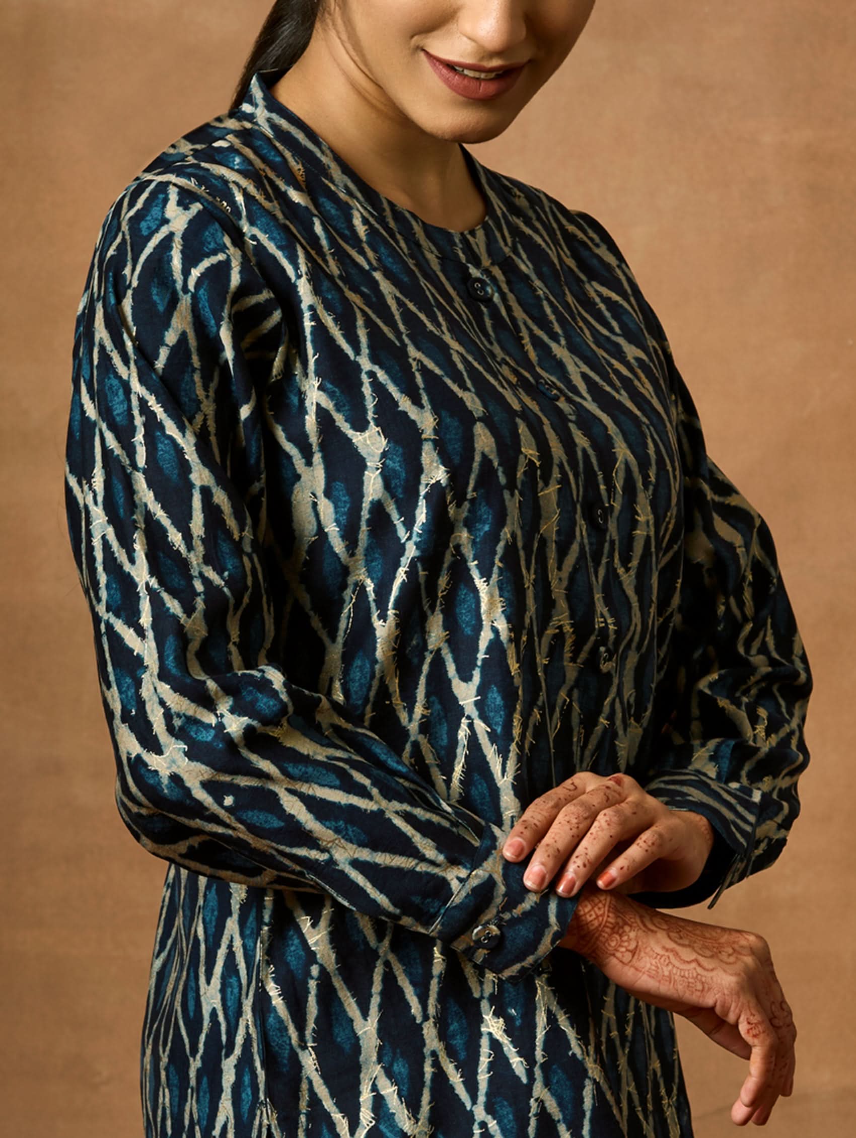 A woman wearing a short kurti with a mandarin collar, full sleeves, and side slits. The kurti is printed with a geometric pattern.