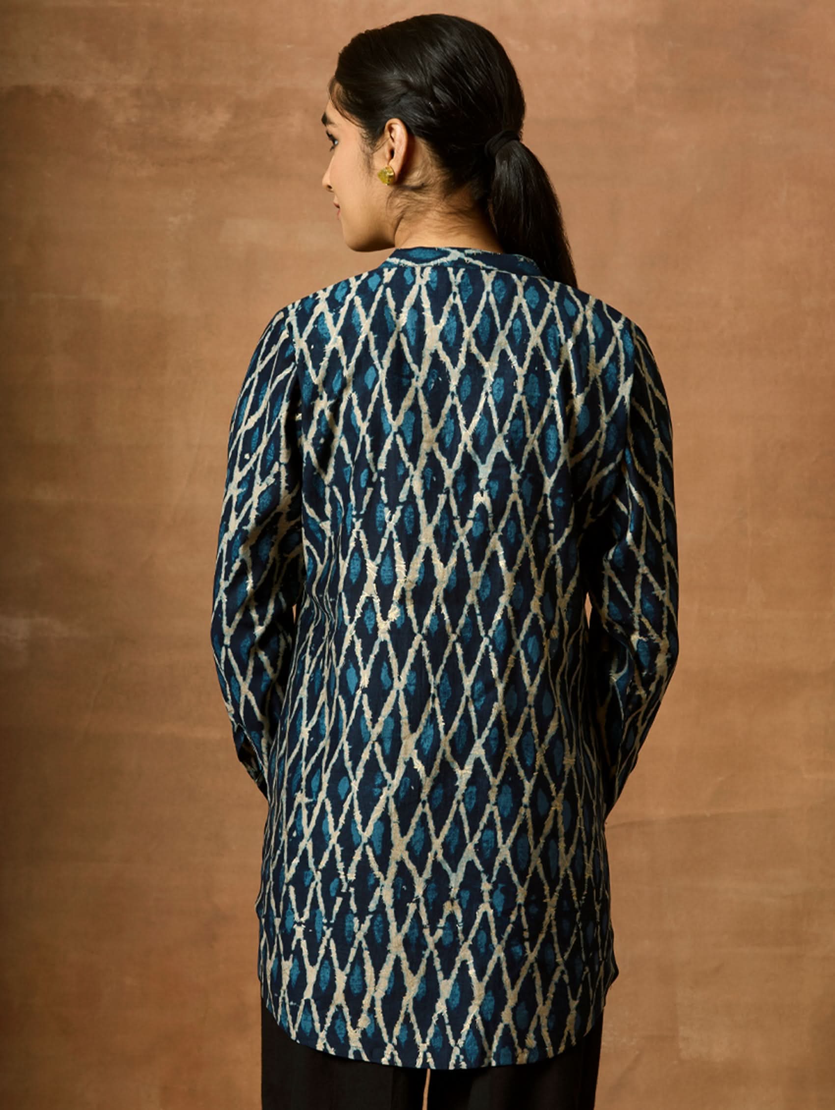 A woman wearing a short kurti with a mandarin collar, full sleeves, and side slits. The kurti is printed with a geometric pattern.