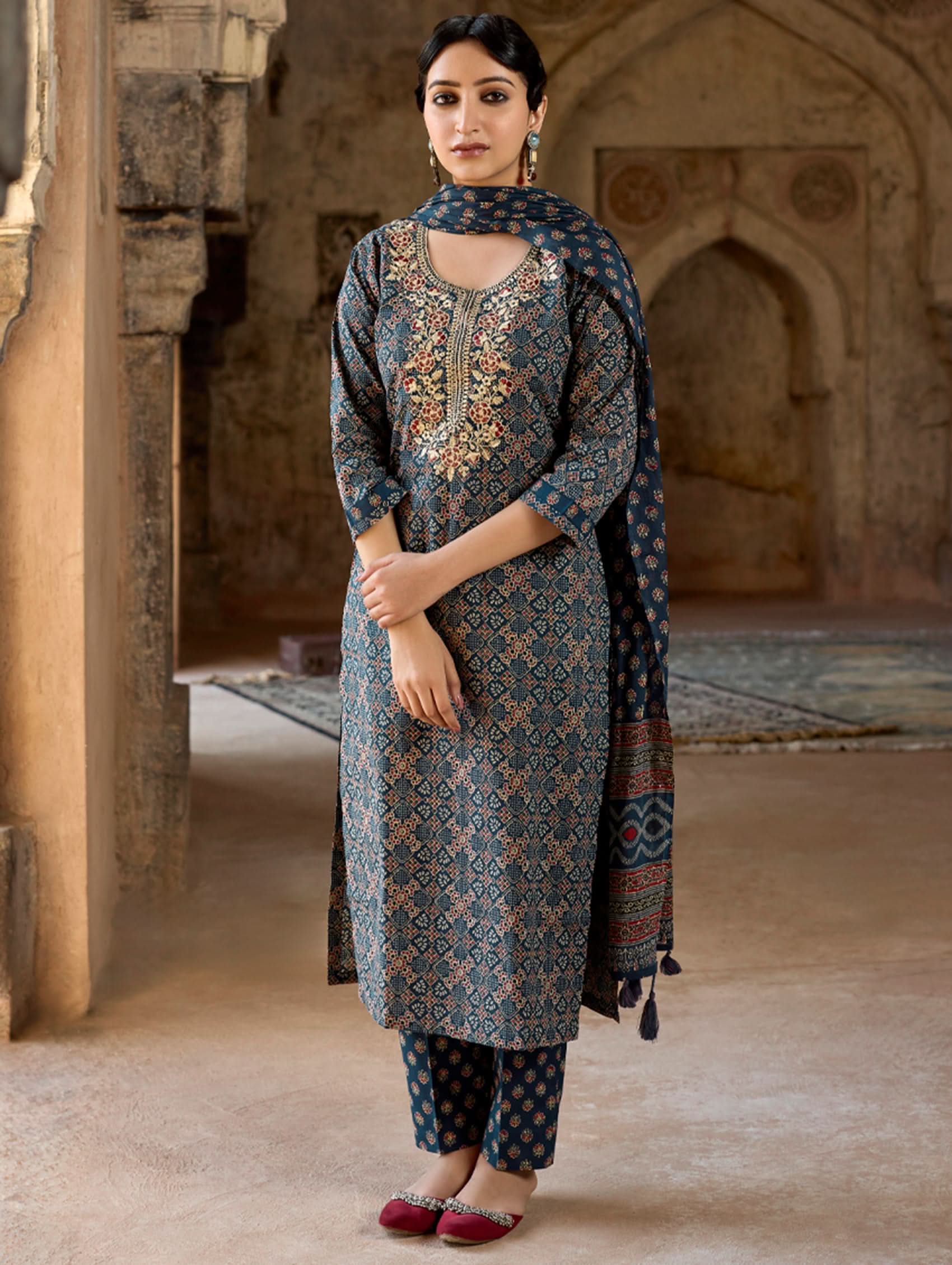 A woman wearing a traditional suit set with embroidered kurta, straight pants, and a printed dupatta.