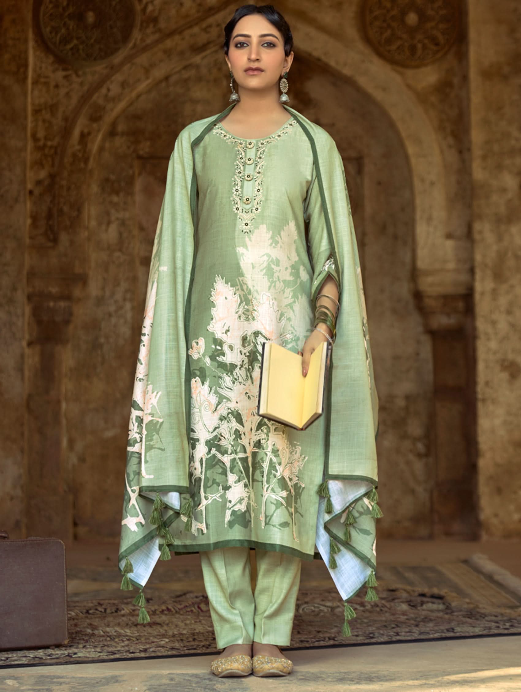 A woman wearing a floral cotton suit set with embroidered details,and printed consisting of a kurta with band collar, pants, and a printed weave cotton dupatta.