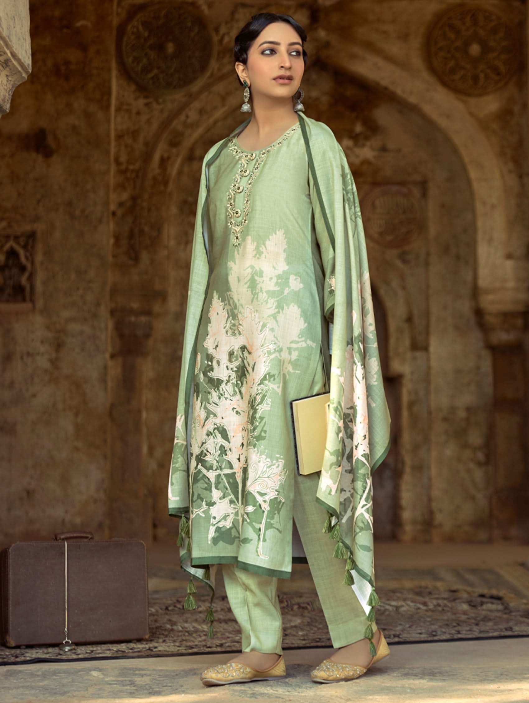A woman wearing a floral cotton suit set with embroidered details,and printed consisting of a kurta with band collar, pants, and a printed weave cotton dupatta.