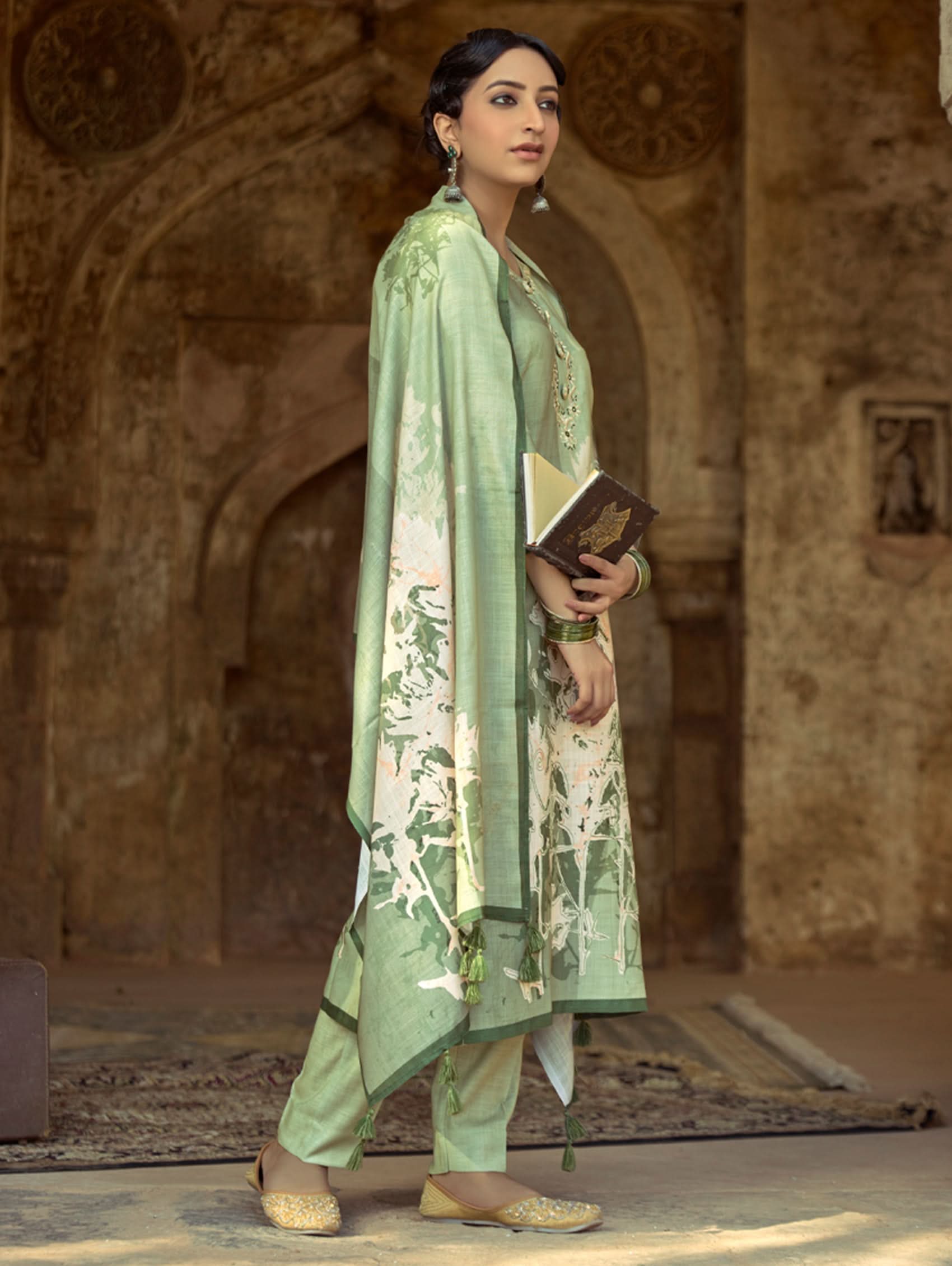 A woman wearing a floral cotton suit set with embroidered details,and printed consisting of a kurta with band collar, pants, and a printed weave cotton dupatta.