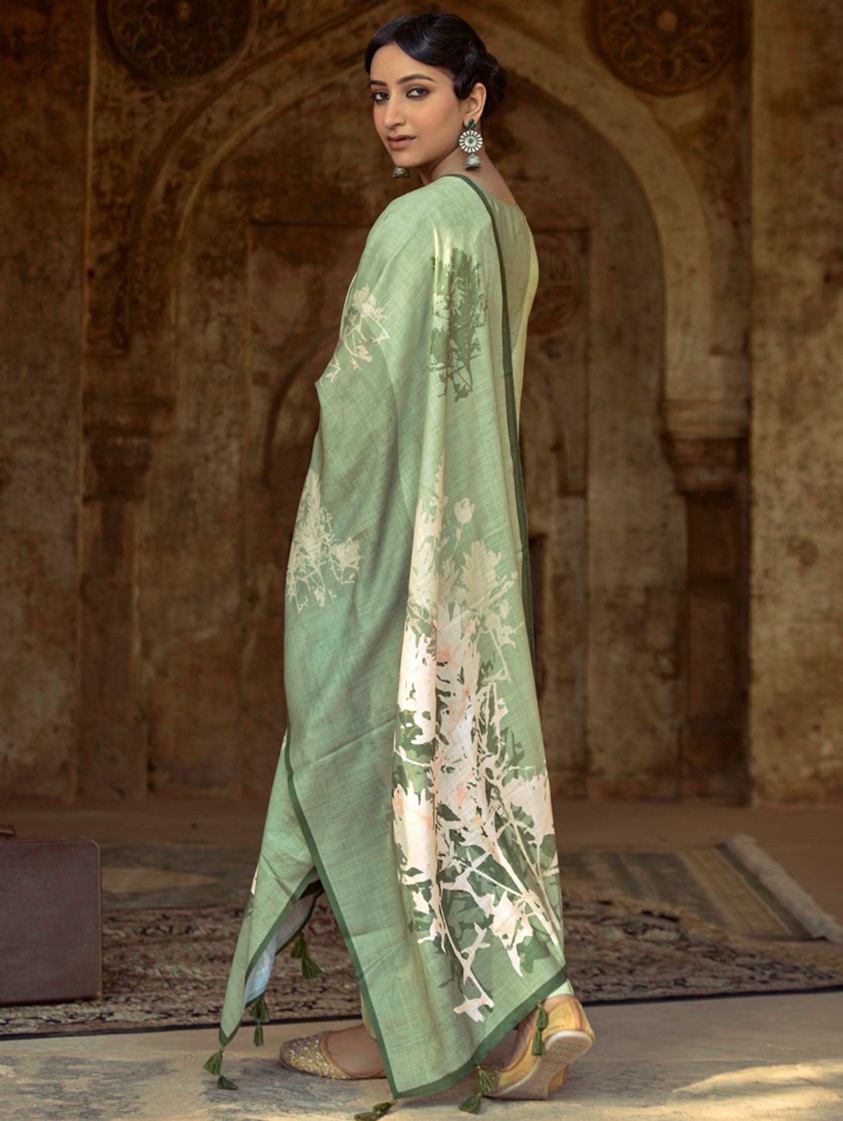 A woman wearing a floral cotton suit set with embroidered details,and printed consisting of a kurta with band collar, pants, and a printed weave cotton dupatta.