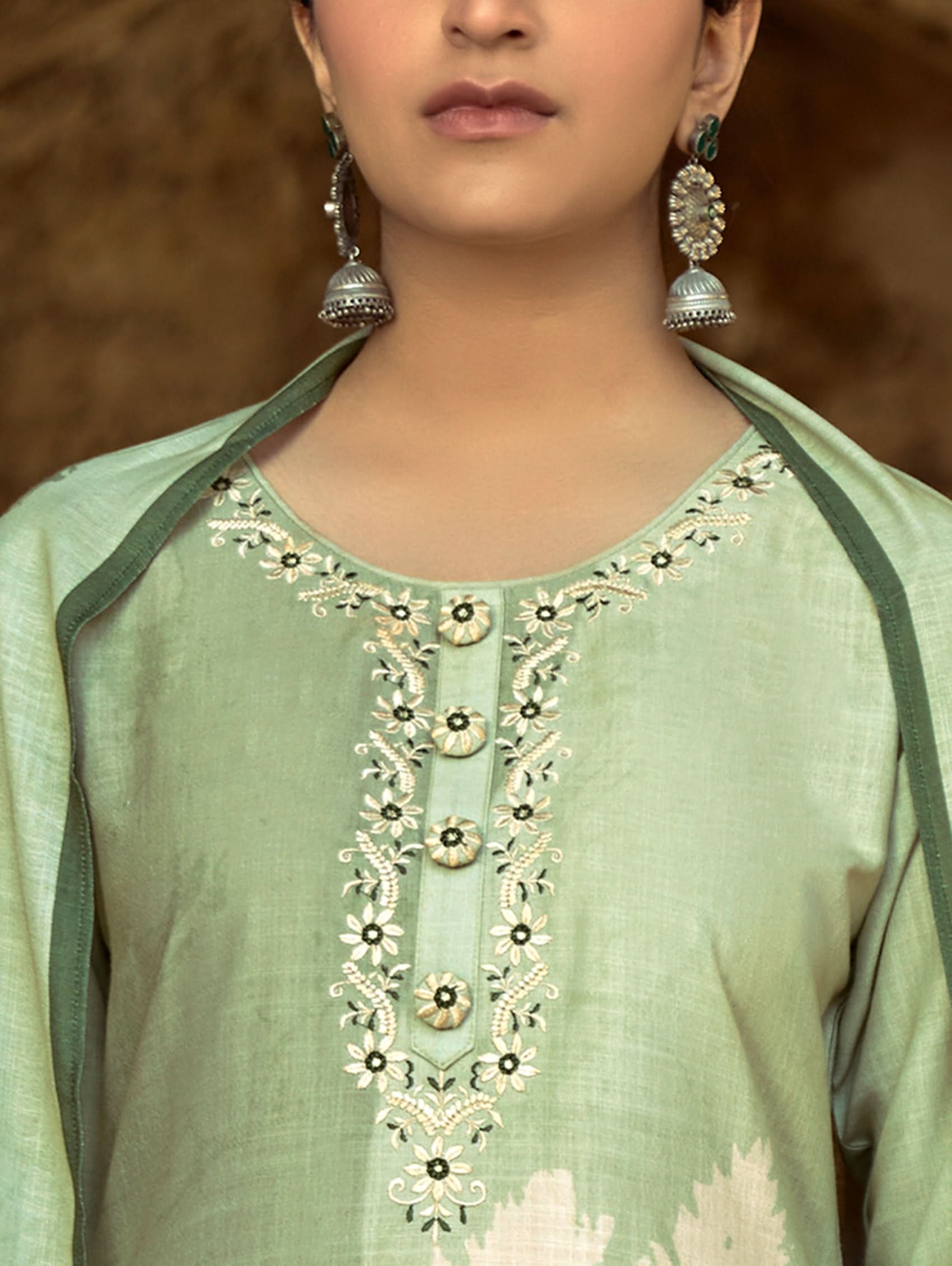 A woman wearing a floral cotton suit set with embroidered details,and printed consisting of a kurta with band collar, pants, and a printed weave cotton dupatta.