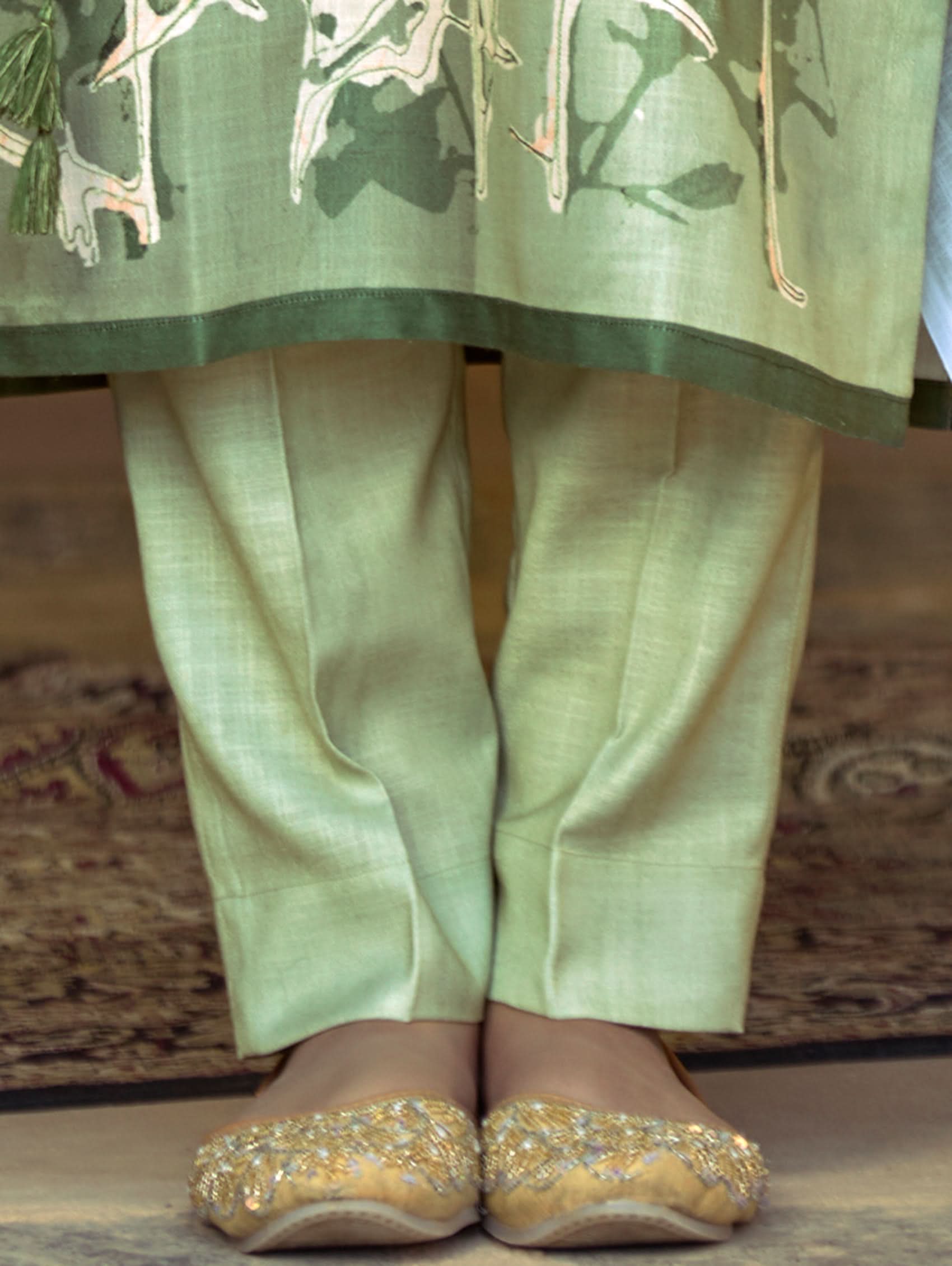 A woman wearing a floral cotton suit set with embroidered details,and printed consisting of a kurta with band collar, pants, and a printed weave cotton dupatta.