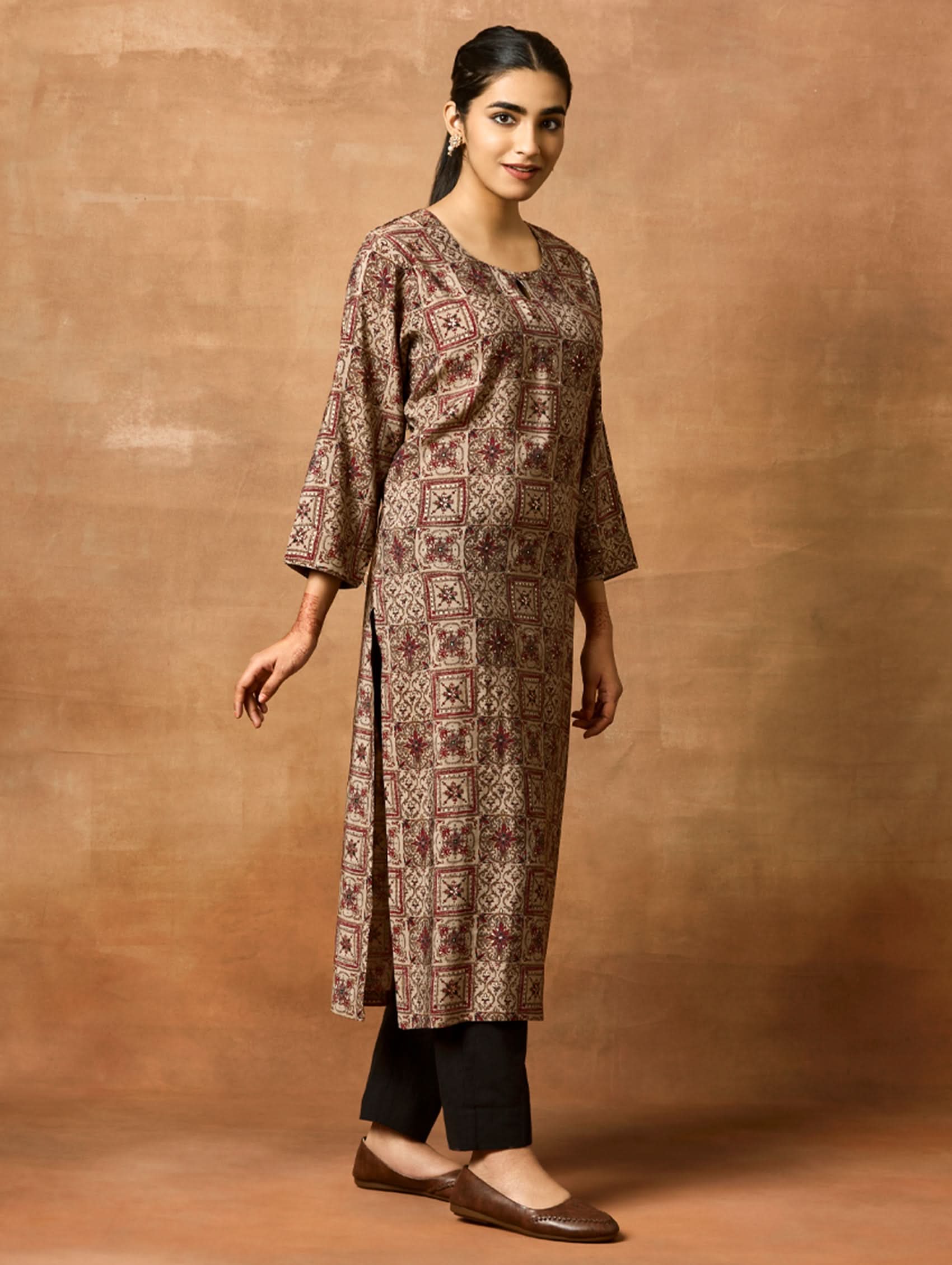 A woman plus size model wearing a brown printed viscose rayon kurta with Keyhole round neckline, three-fourth sleeves, and side slits.
