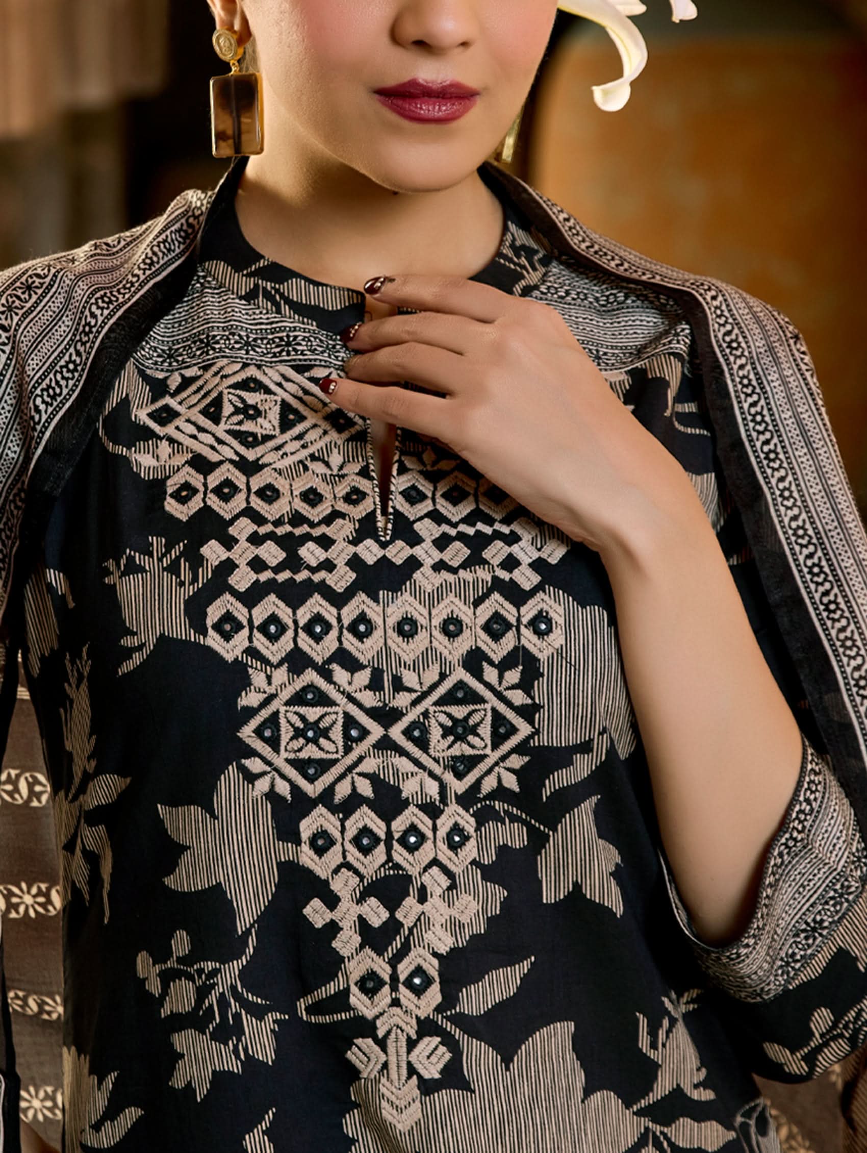 A woman wearing a floral cotton suit set with embroidered details,and printed consisting of a kurta with band collar, pants, and a printed weave silk dupatta.