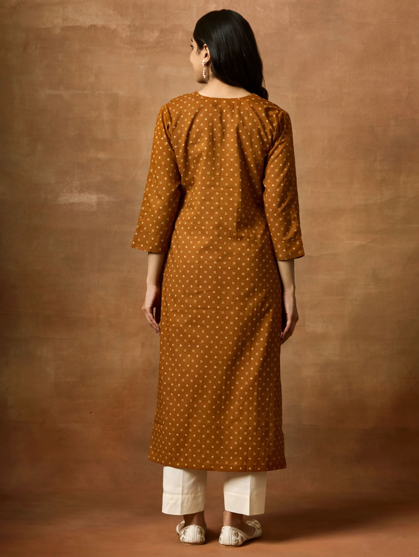 Person wearing a brown polka dot kurta against a brown background
