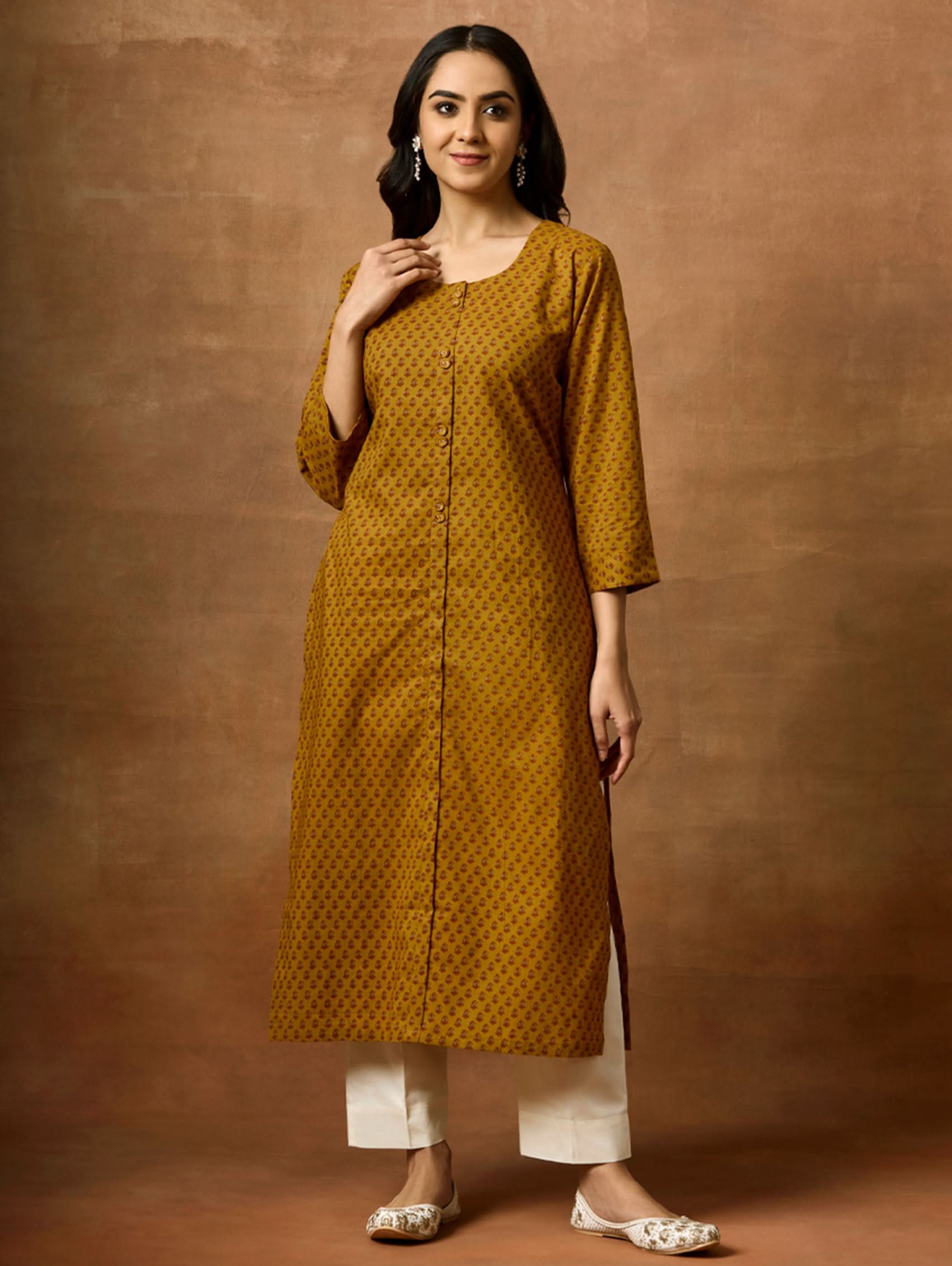 A woman wearing a yellow printed pure cotton kurta with round neckline, three-fourth sleeves, and side slits.