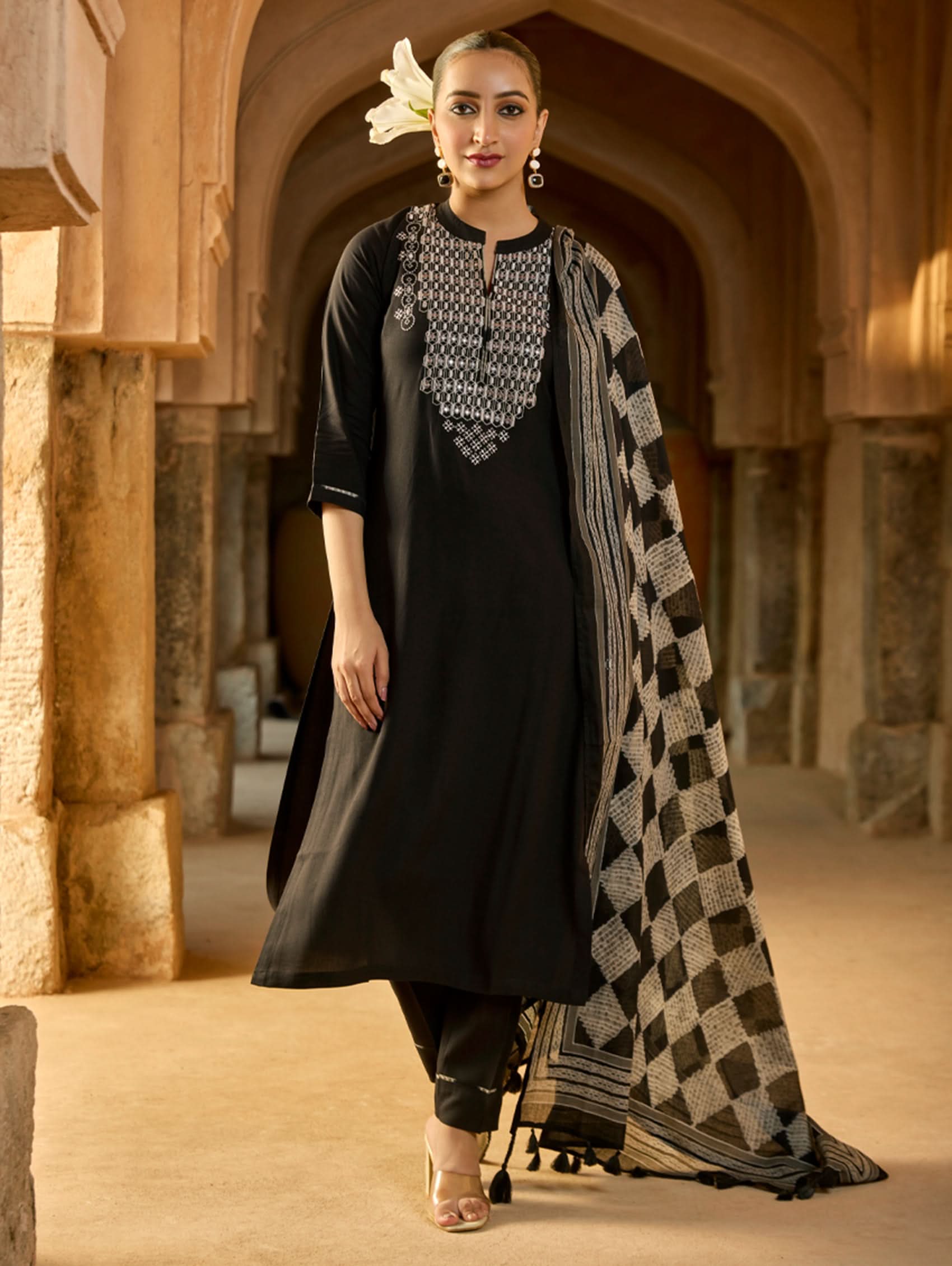 A woman wearing a black viscose rayon suit set with embroidery on the kurta, consisting of a kurta, pants, and a printed dupatta.