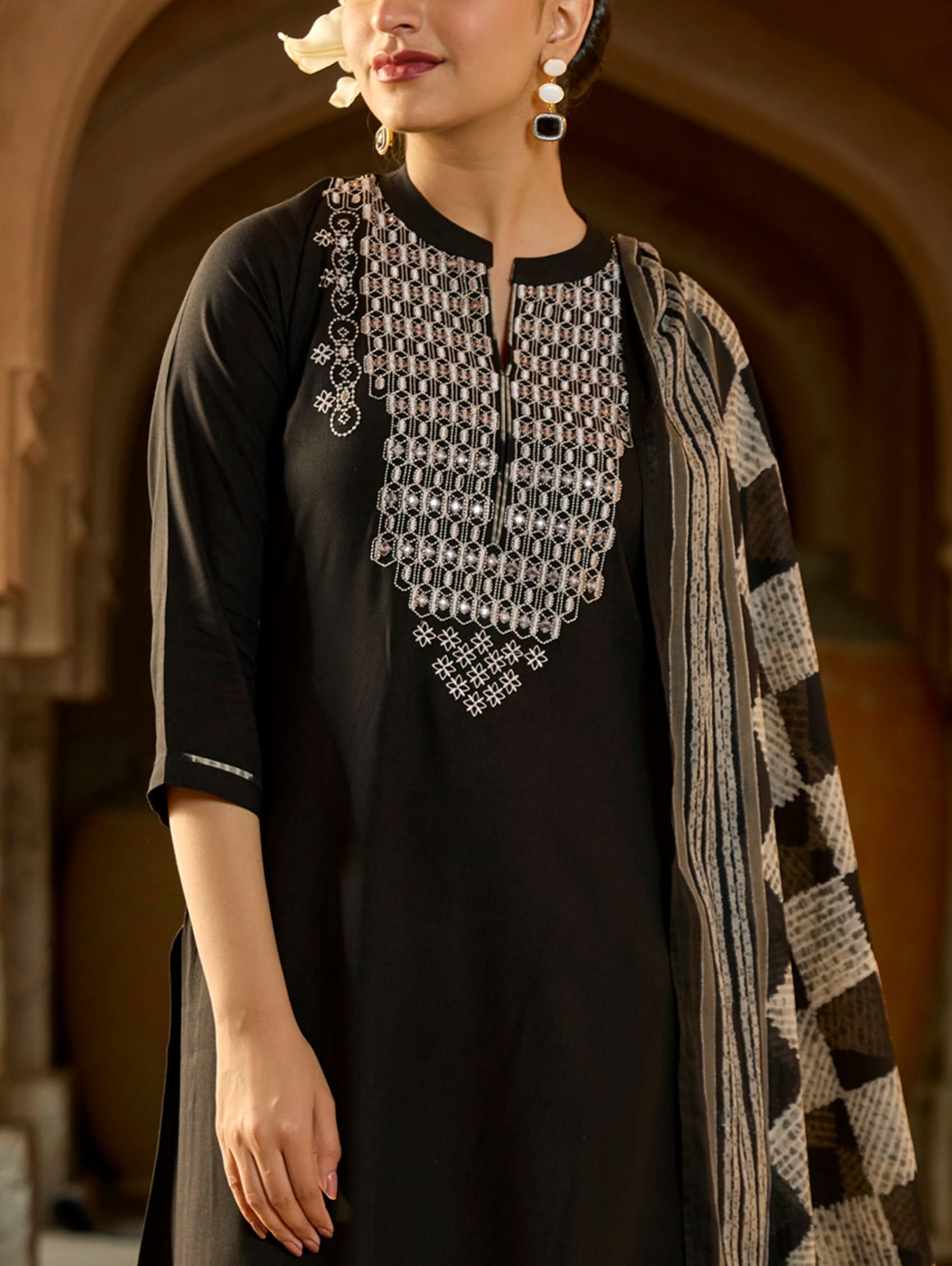A woman wearing a black viscose rayon suit set with embroidery on the kurta, consisting of a kurta, pants, and a printed dupatta.