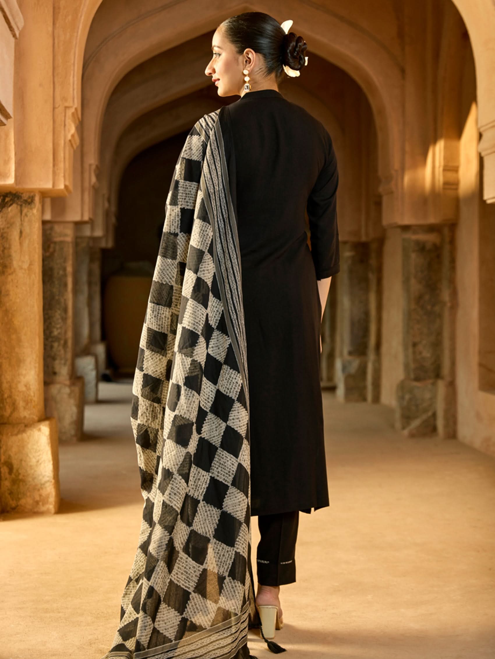 A woman wearing a black viscose rayon suit set with embroidery on the kurta, consisting of a kurta, pants, and a printed dupatta.