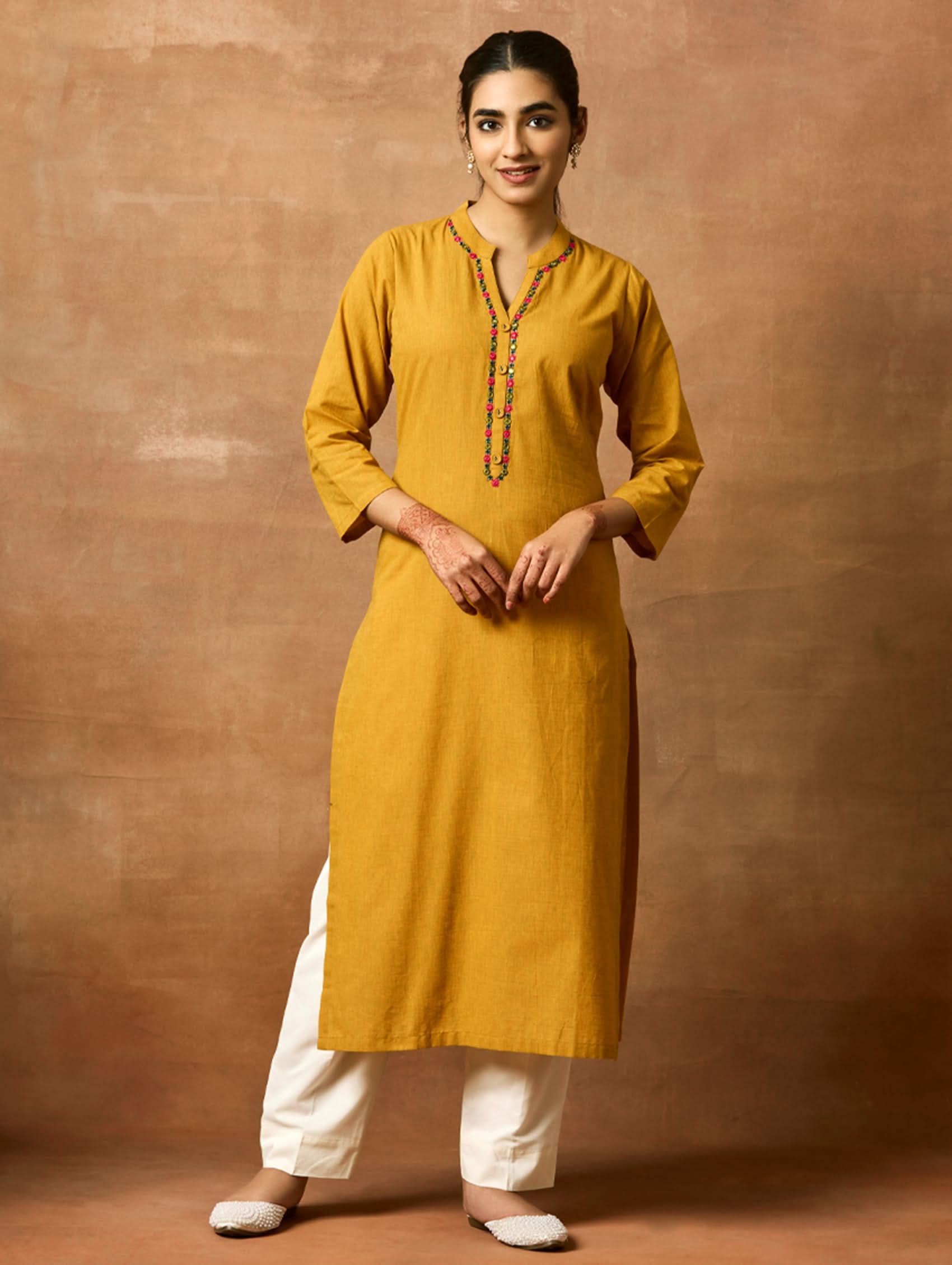 A woman plus size model wearing a yellow kurta with a ban collar, three-fourth sleeves, and side slits. The kurta has computerised thread embroidery on it.