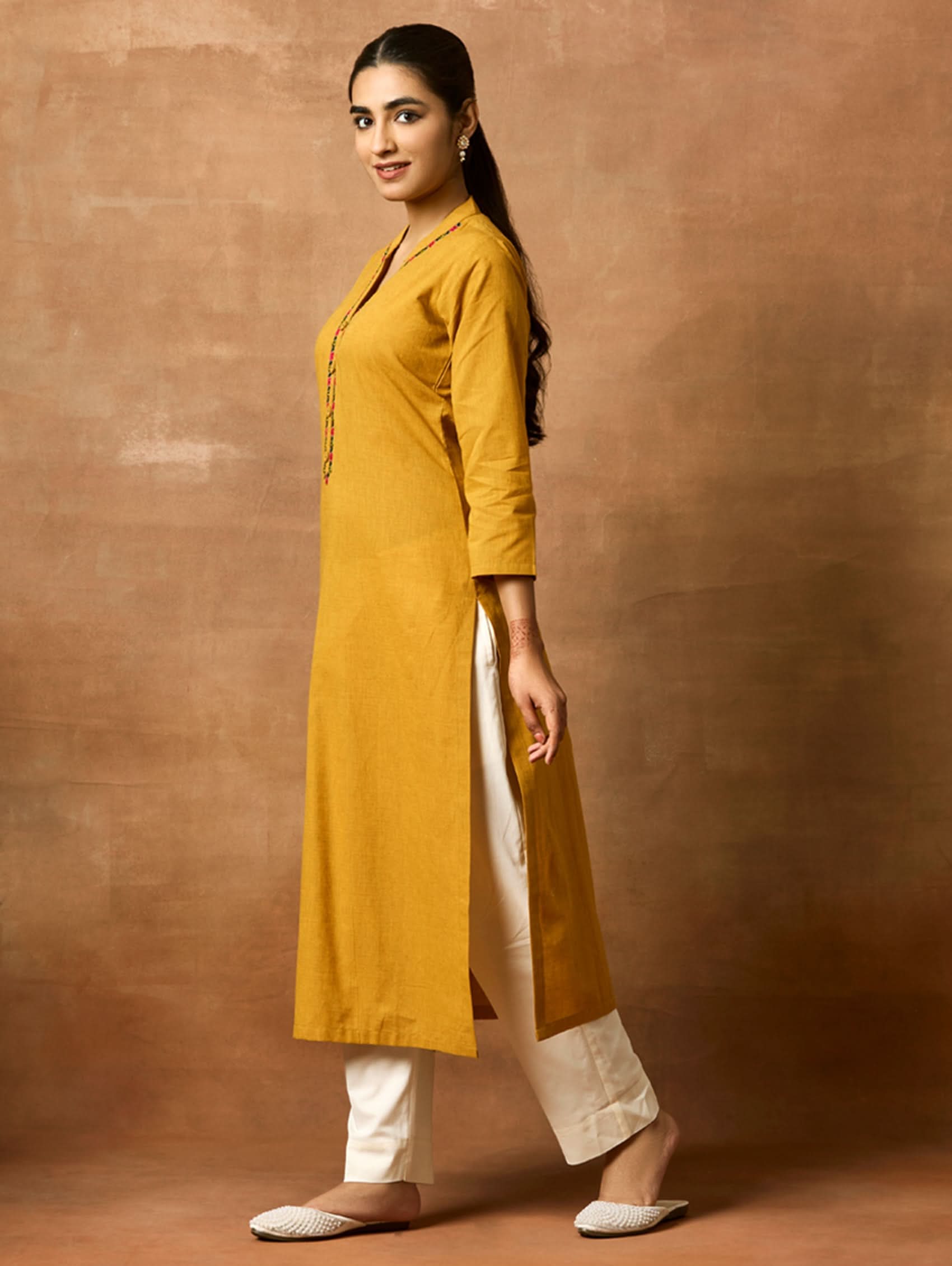 A woman plus size model wearing a yellow kurta with a ban collar, three-fourth sleeves, and side slits. The kurta has computerised thread embroidery on it.