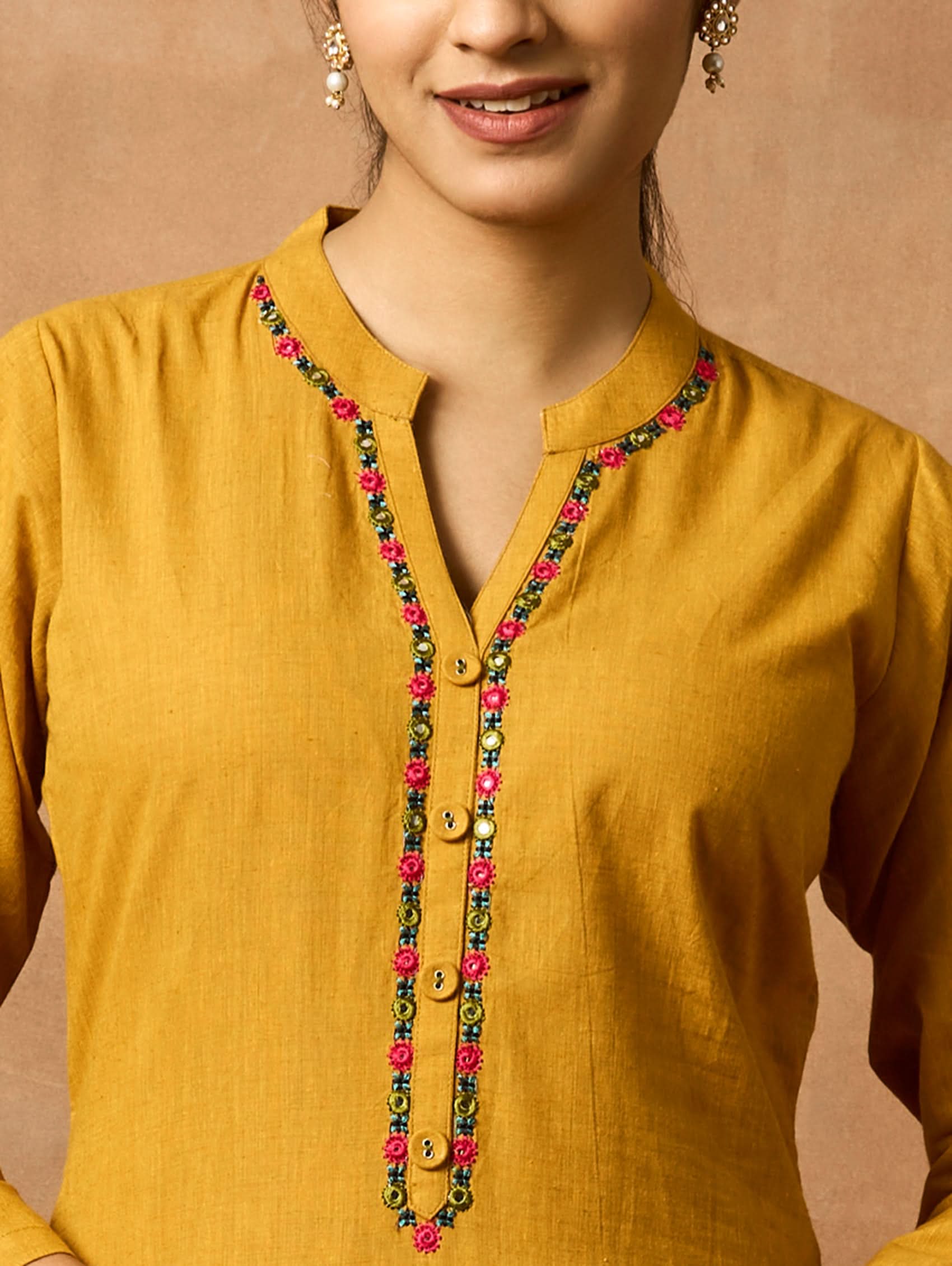 A woman plus size model wearing a yellow kurta with a ban collar, three-fourth sleeves, and side slits. The kurta has computerised thread embroidery on it.