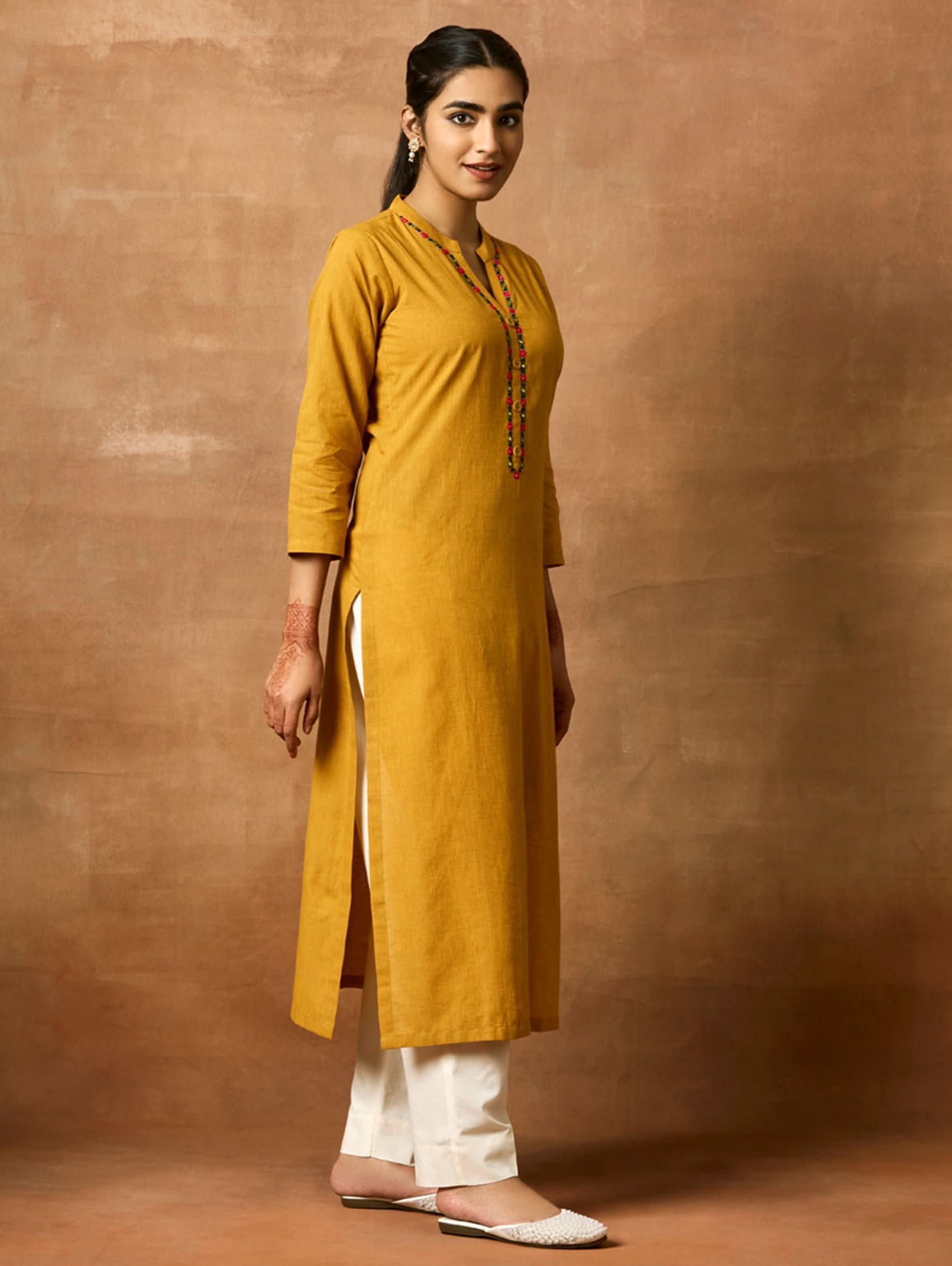 A woman plus size model wearing a yellow kurta with a ban collar, three-fourth sleeves, and side slits. The kurta has computerised thread embroidery on it.