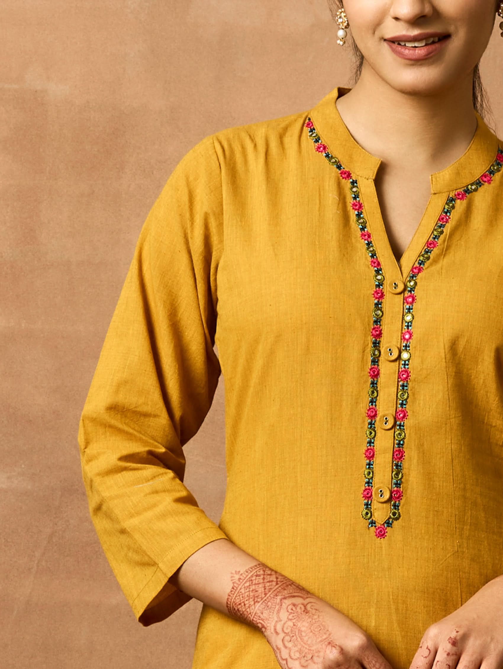 A woman plus size model wearing a yellow kurta with a ban collar, three-fourth sleeves, and side slits. The kurta has computerised thread embroidery on it.