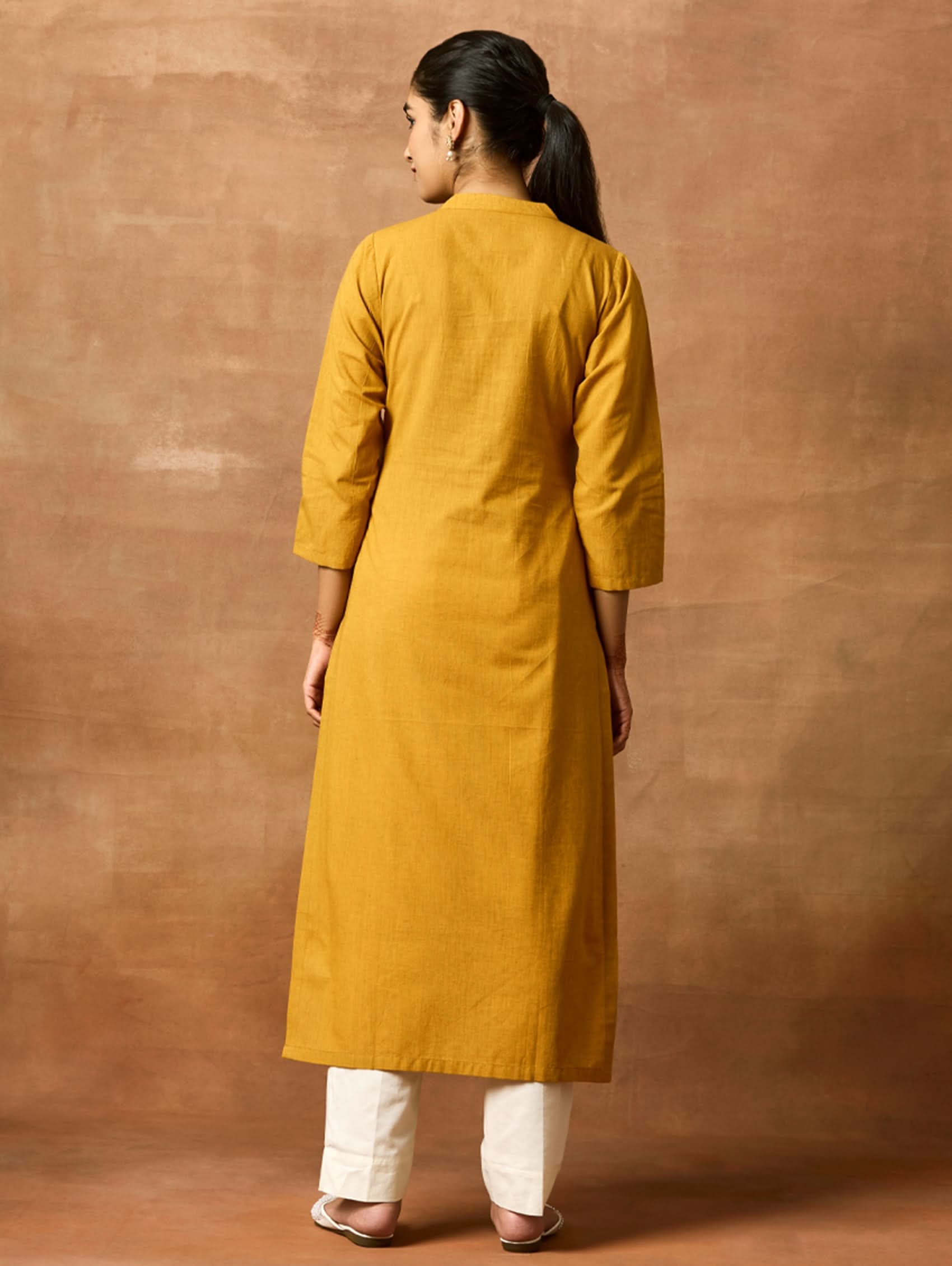 A woman plus size model wearing a yellow kurta with a ban collar, three-fourth sleeves, and side slits. The kurta has computerised thread embroidery on it.