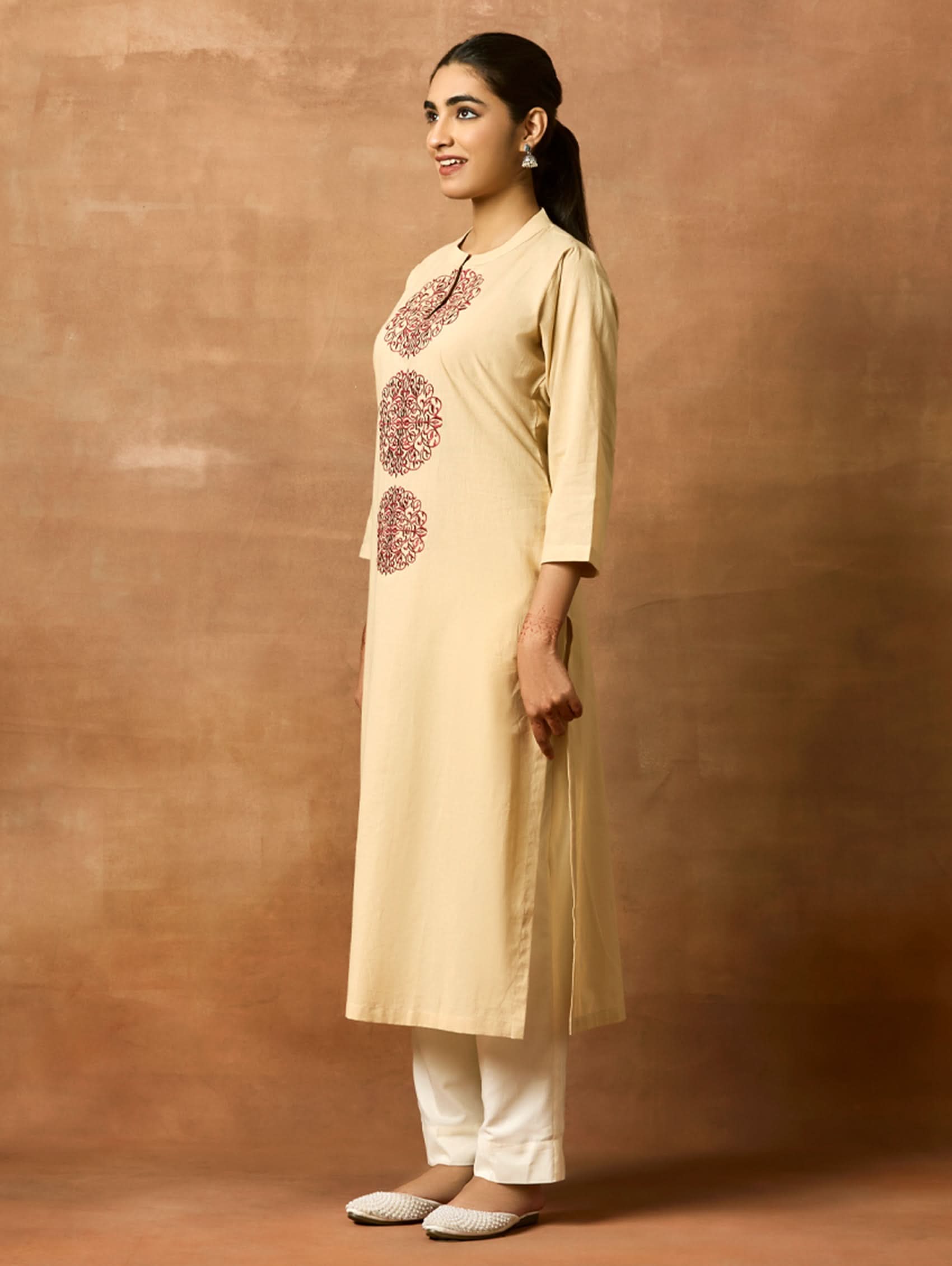 A woman plus-size model wearing a beige kurta with ban collar and three-fourth sleeves, featuring computerised thread embroidery.