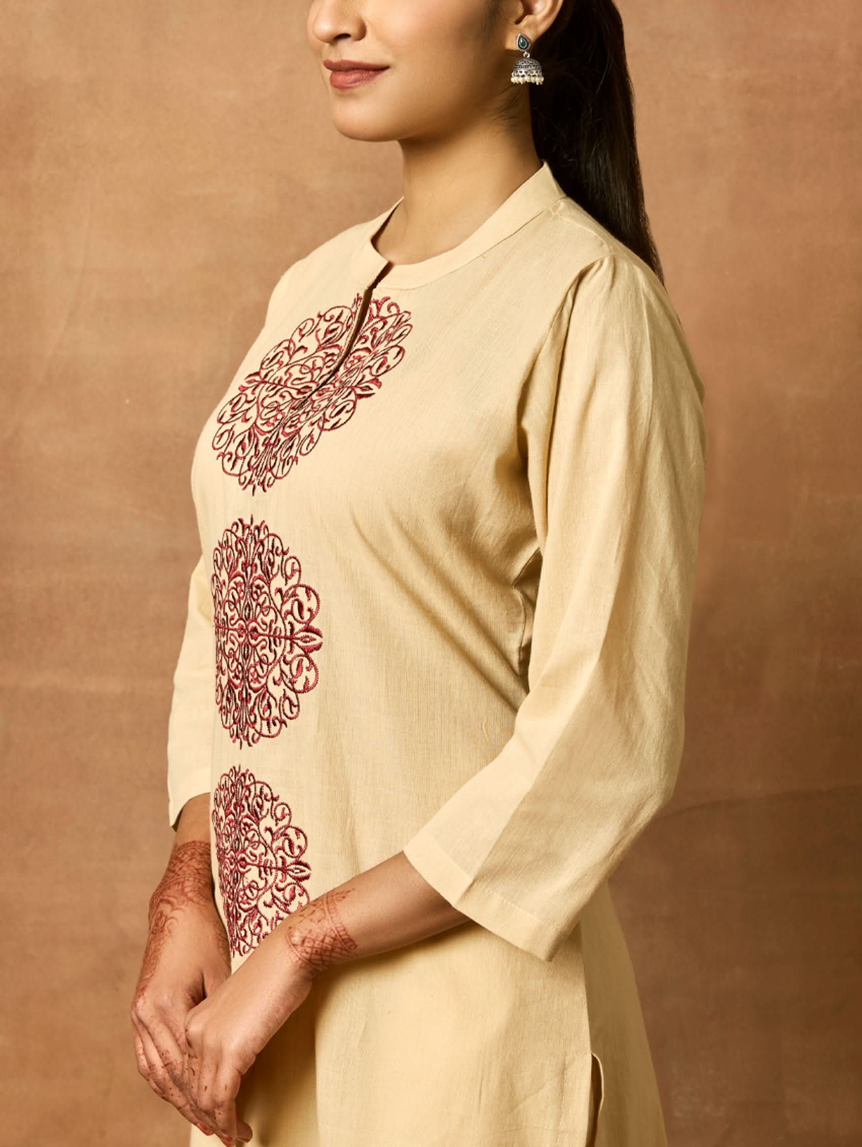 A woman plus-size model wearing a beige kurta with ban collar and three-fourth sleeves, featuring computerised thread embroidery.